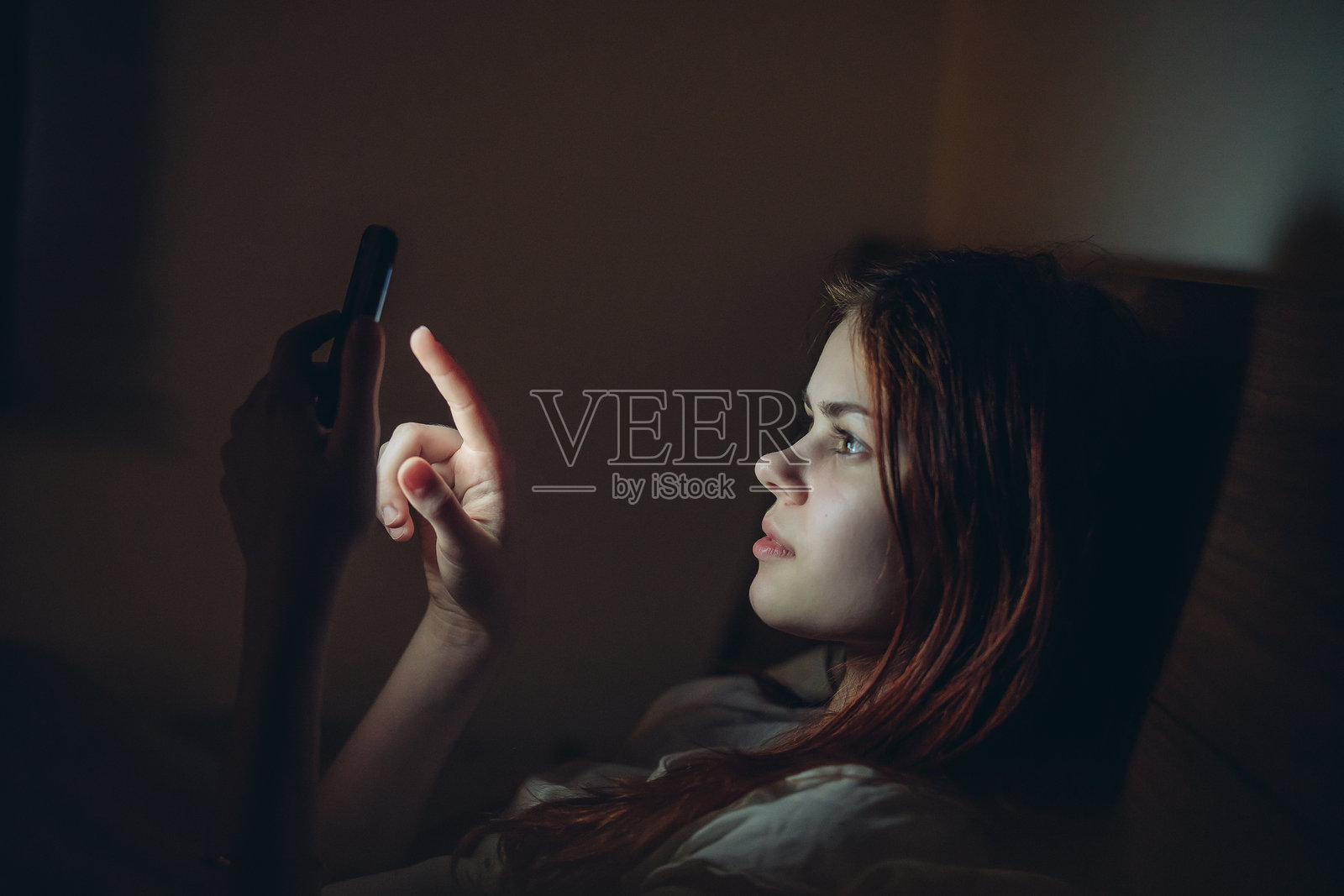 晚上躺在床上的女人手里拿着手机，展现生活方式。照片摄影图片