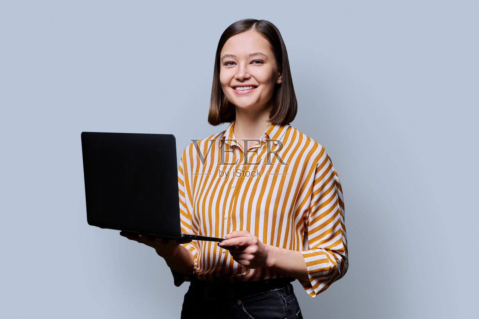 微笑的年轻女性在灰色工作室背景前使用笔记本电脑照片摄影图片