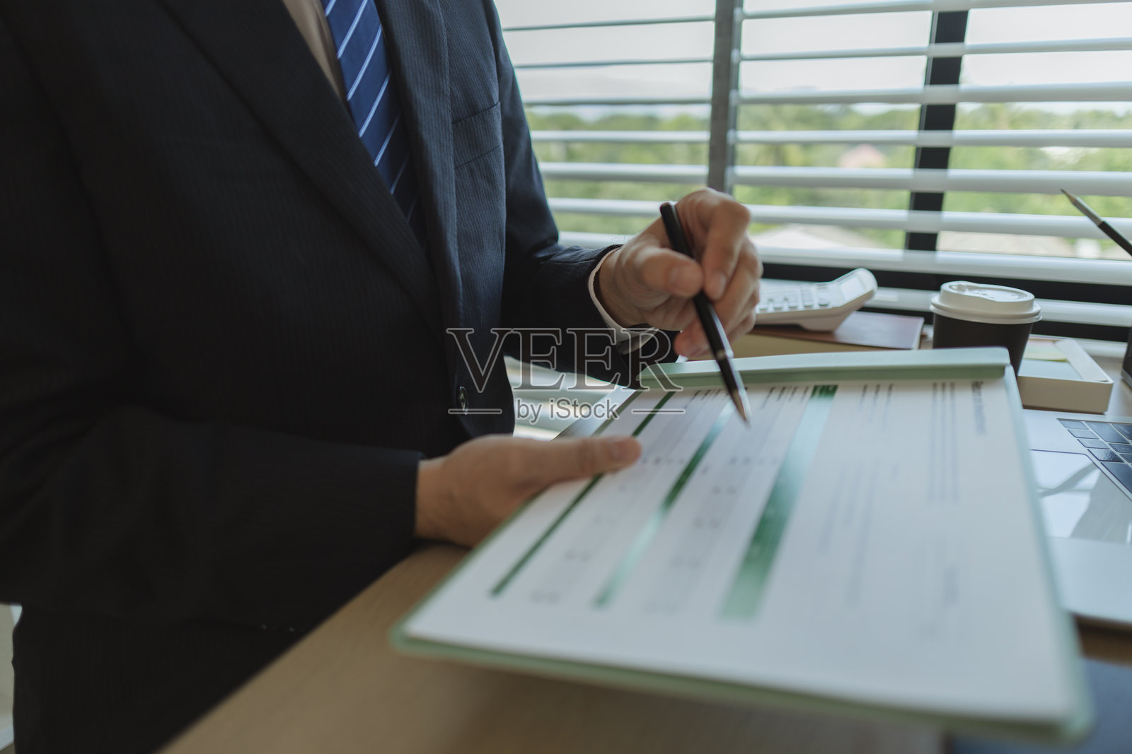 一位商人在办公室里坐着，手中拿着文件以分析数据。一位公司的高管穿着西装，显得庄重，以展示他作为公司所有者的身份。照片摄影图片