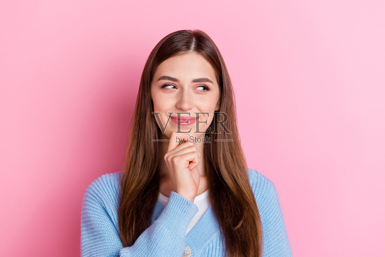 一位时尚可爱的女孩，长发披肩，手托下巴，目光空洞，背景为粉色。照片摄影图片