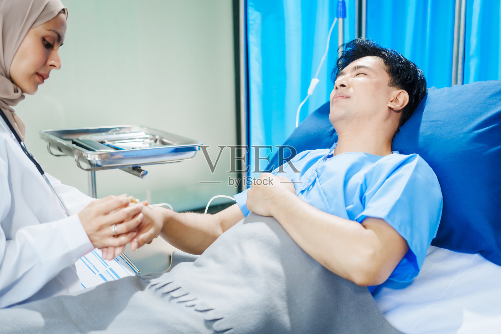 两位穆斯林女医生在医院检查一名躺在床上的男性患者的病史和症状，监测他的恢复和健康状况。照片摄影图片