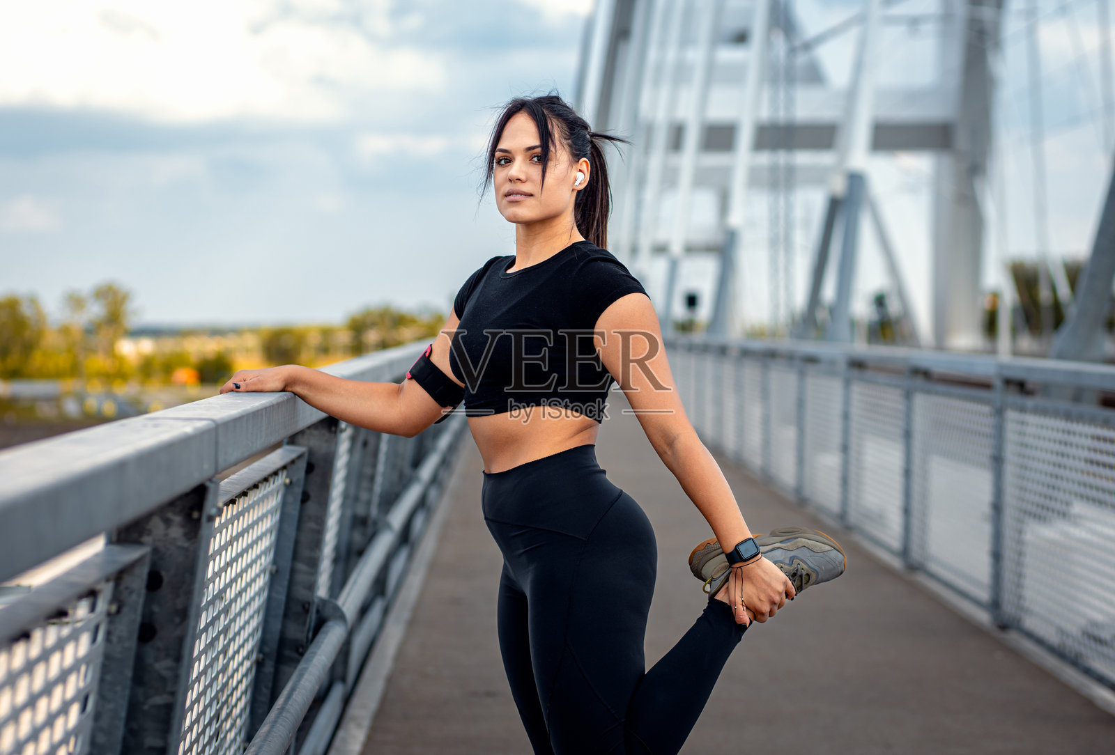 年轻的健身女性穿着黑色运动服，在桥上拉伸肌肉为跑步做准备。照片摄影图片