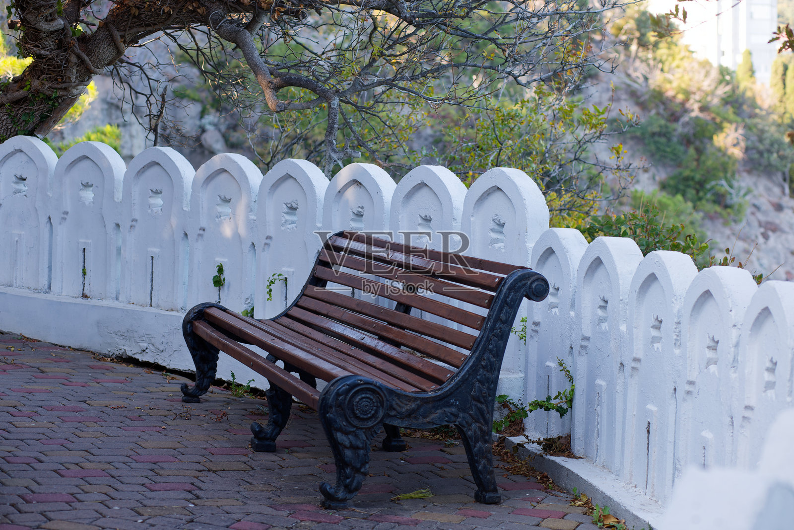木制长椅坐落在白墙旁的砖石人行道上照片摄影图片