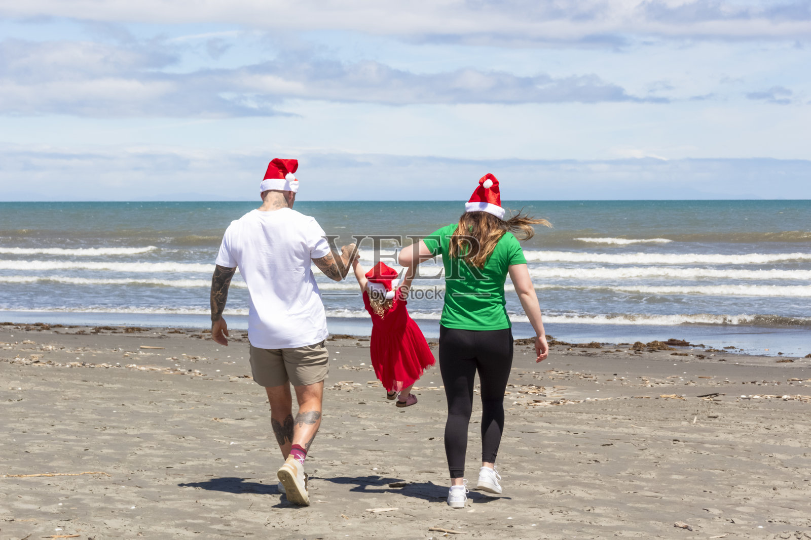 一个年轻家庭在圣诞节时穿着圣诞老人帽子，在海滩上共度美好时光。照片摄影图片