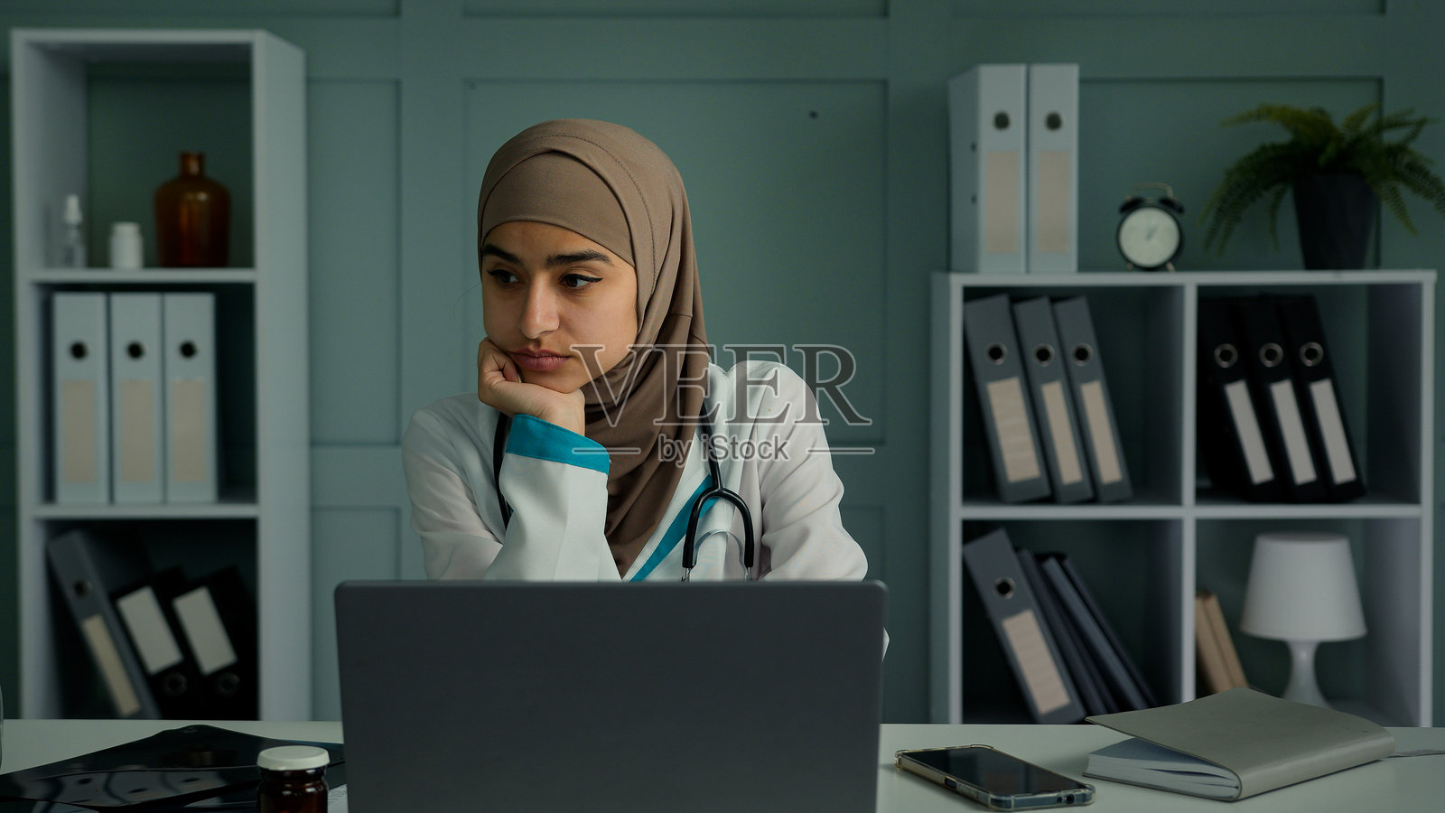 沉思的年轻女治疗师坐在诊所里，感到孤独、忧伤和无聊，担心自己缺乏动力，懒散的女医生或医学生思考着心理疲惫、抑郁和健康问题。照片摄影图片