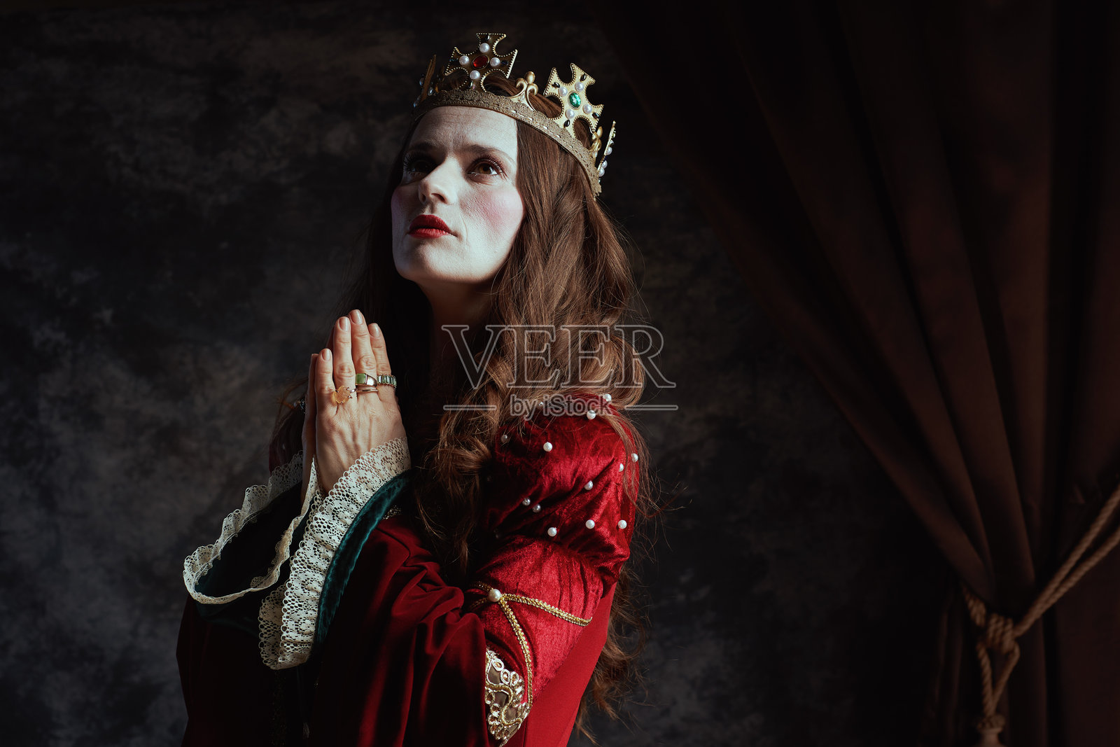 穿着红色裙子和王冠的中世纪女王在祈祷照片摄影图片