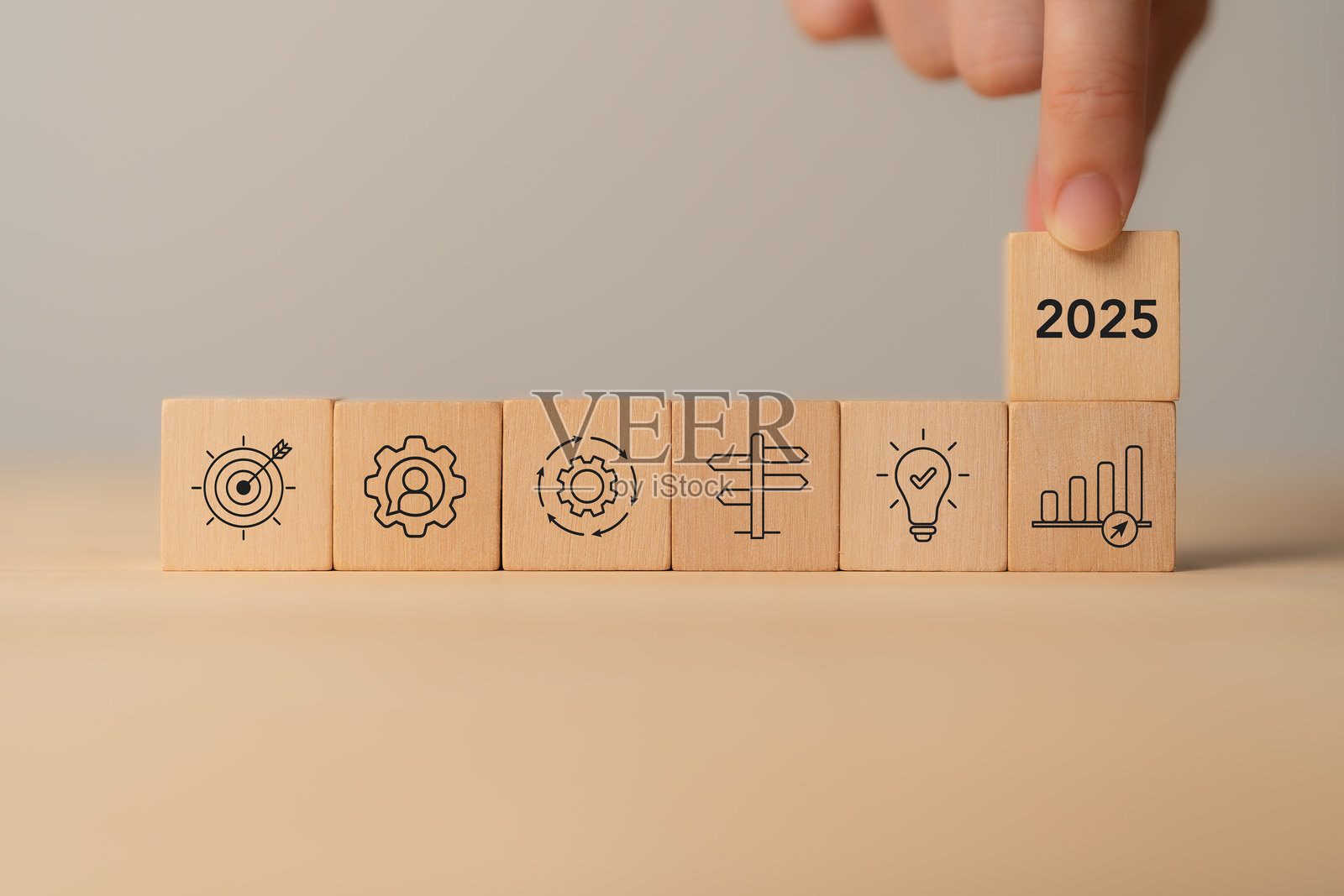 商业规划，2025年的新年计划。木块上有代表商业目标、创新和增长的图标，一只手将标有“2025”的木块放置上去，象征着未来的战略和规划。照片摄影图片