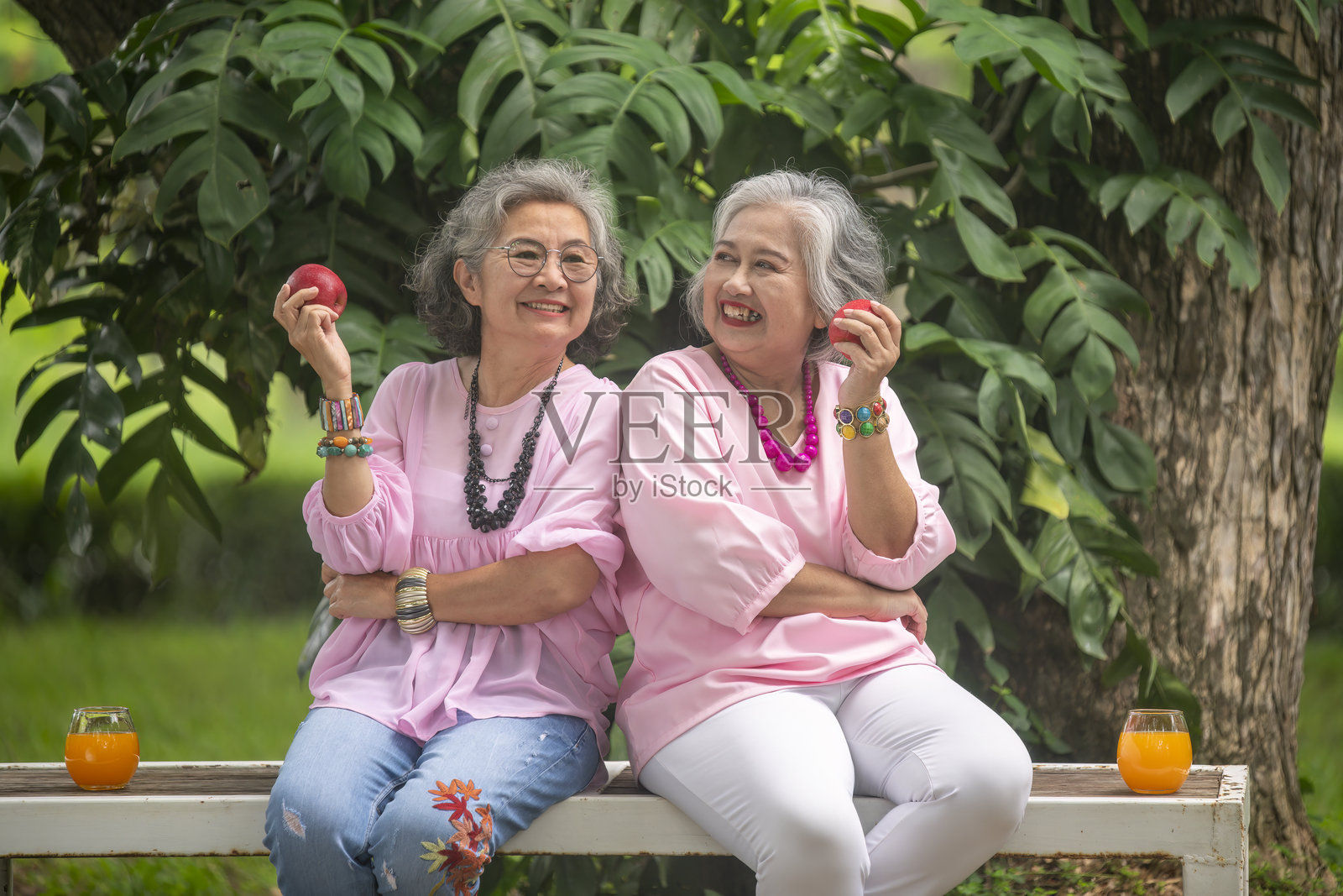 两位老年女性坐在户外，享用新鲜的苹果和橙汁，享受假日生活方式的健康放松时光。照片摄影图片