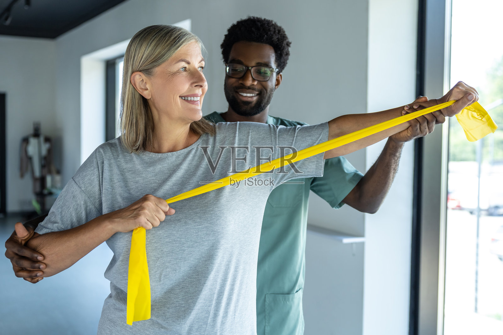 医生在康复治疗中帮助患者拉伸手臂，使用阻力带进行创伤恢复。照片摄影图片