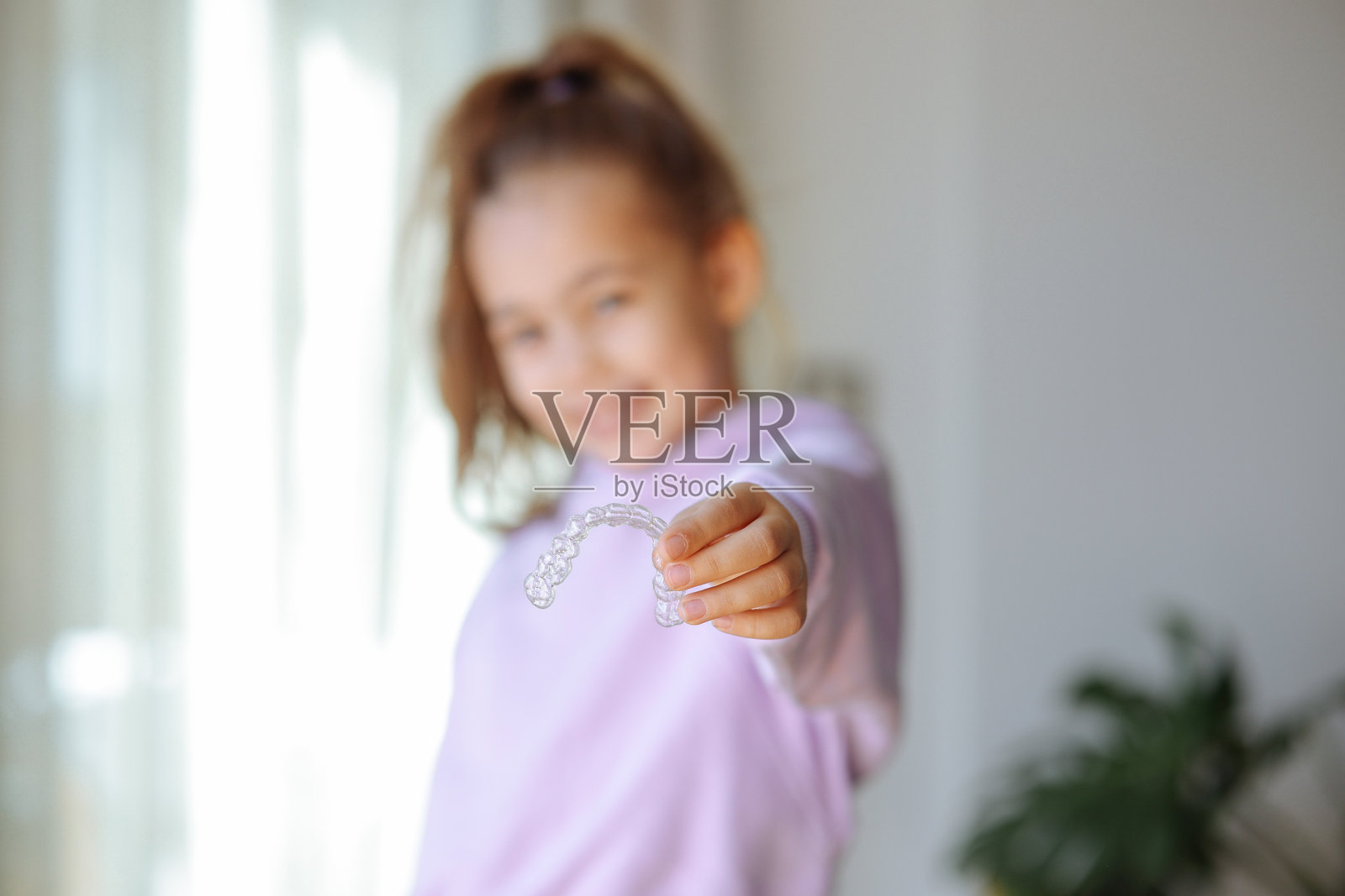 微笑的小女孩在白色背景的摄影棚中手持牙套，牙科保健和正畸概念。照片摄影图片