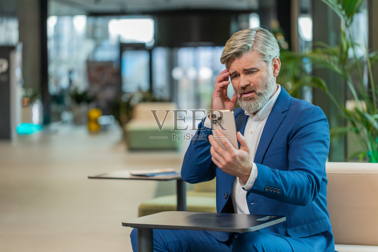 成熟的商人在酒店大堂使用智能手机，突然对彩票结果感到震惊照片摄影图片