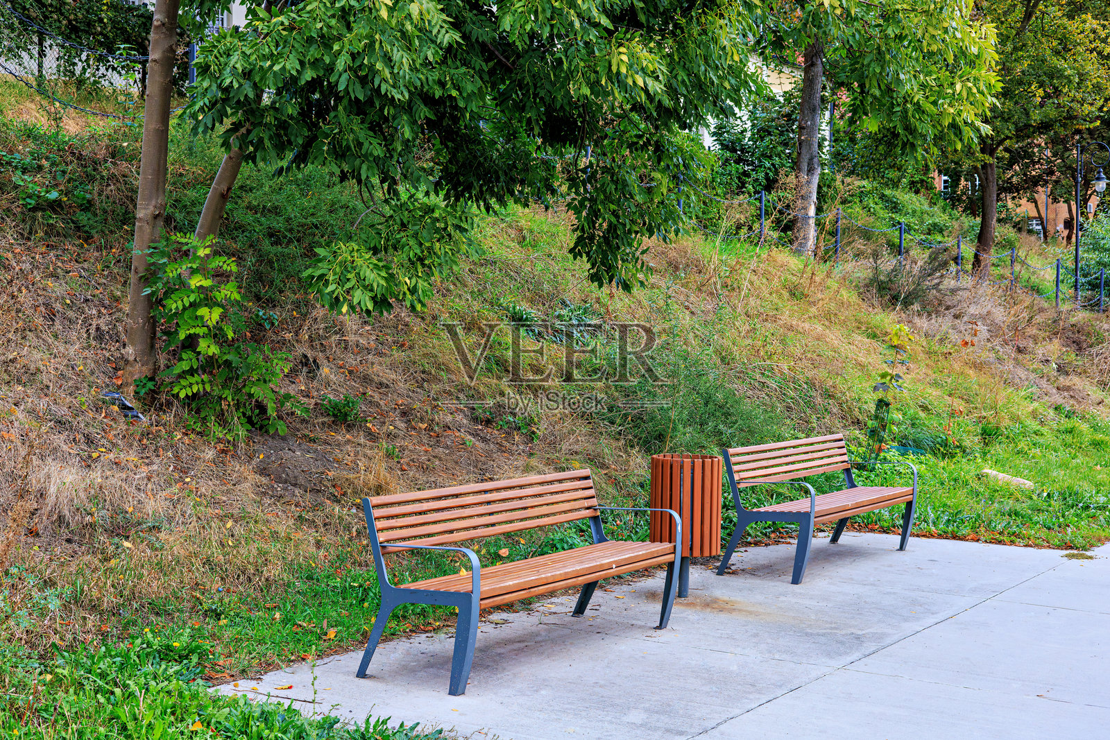公园小径上的两张长椅和一个垃圾桶。照片摄影图片