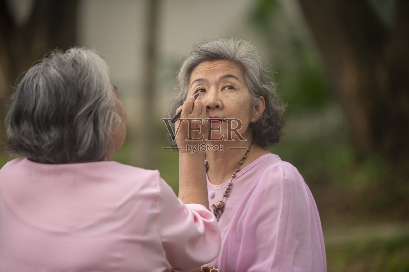 老年女性坐在郁郁葱葱的花园里，进行化妆，桌上摆放着小镜子和各种化妆品，这是老年人放松时光和友好关系的概念。照片摄影图片