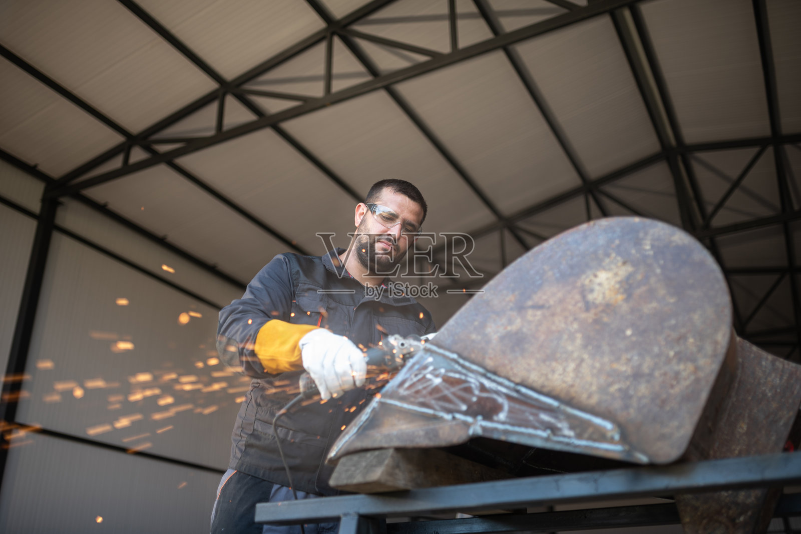 金属工人在车间用角磨机切割金属，产生火花照片摄影图片