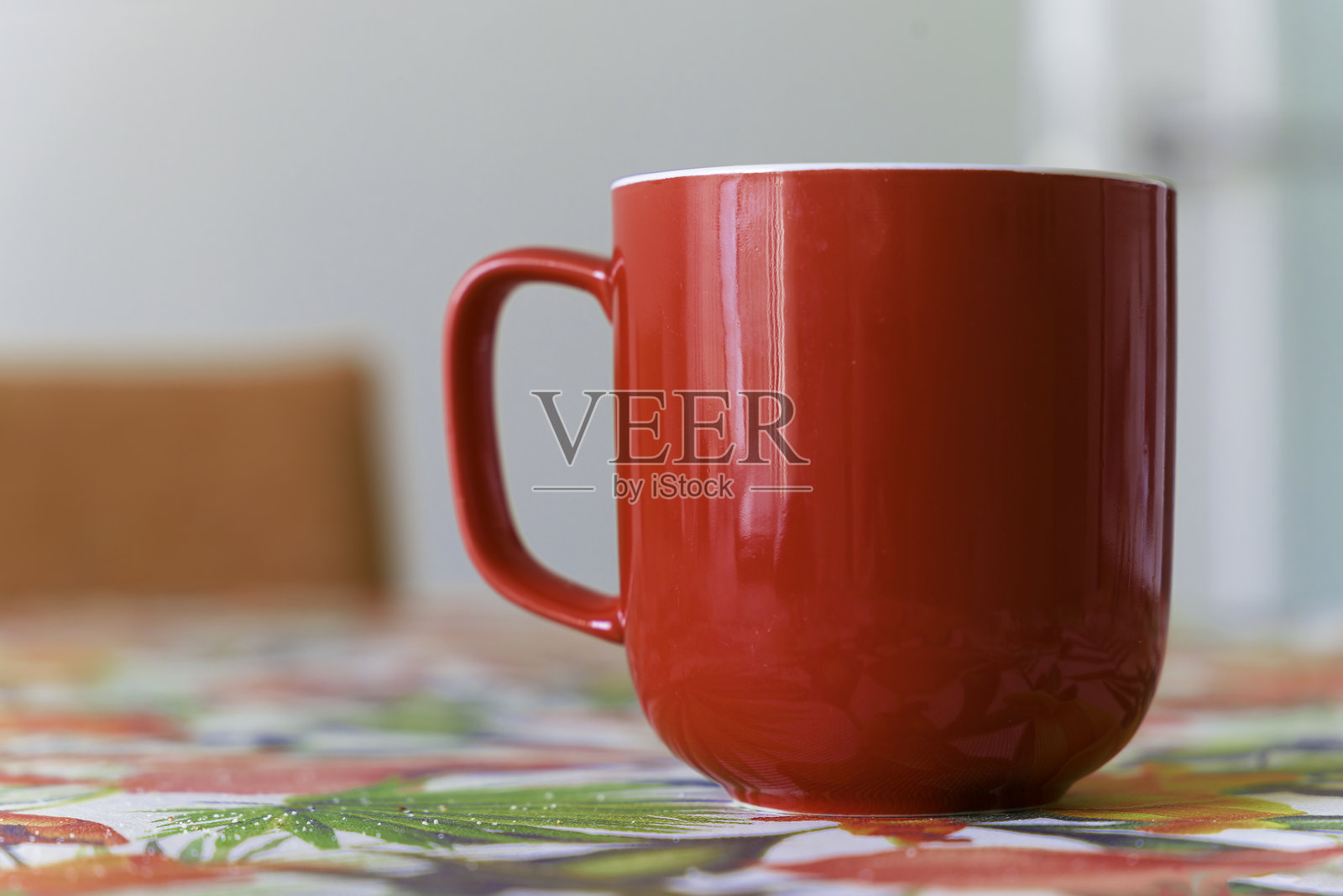 一只红色咖啡杯放在一张色彩斑斓的桌布上。照片摄影图片