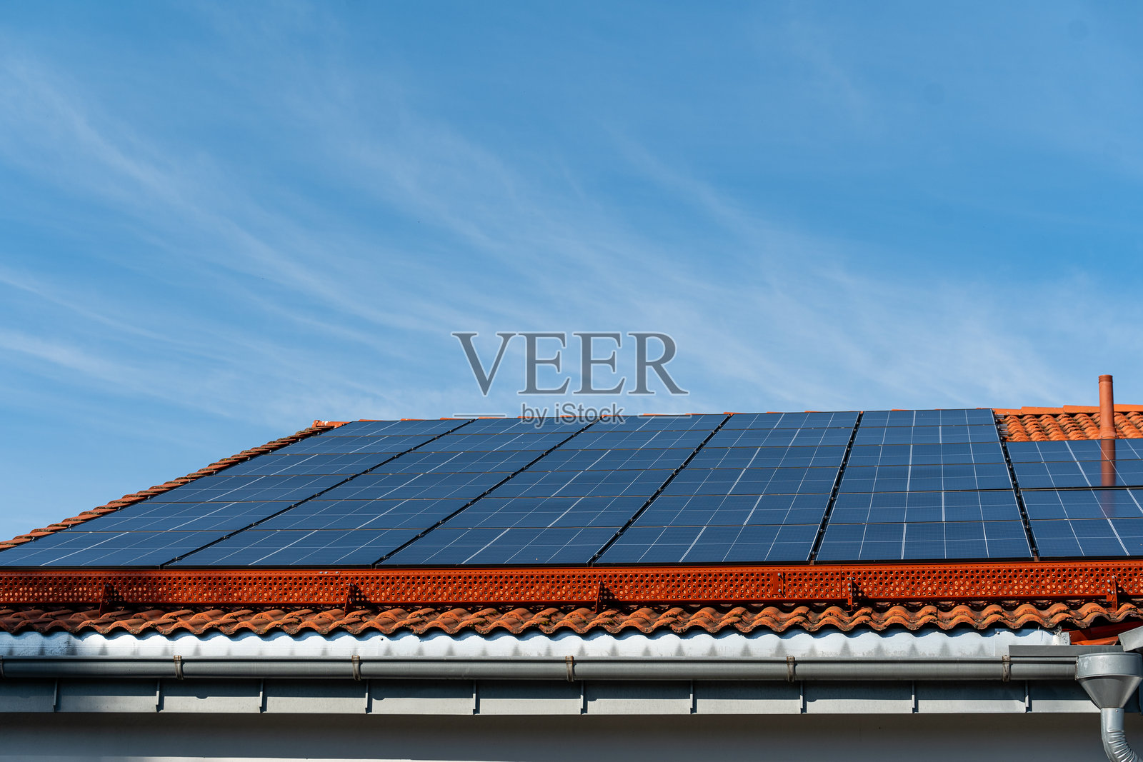 阳光明媚的蓝天上，屋顶上装满了一排太阳能电池板。照片摄影图片