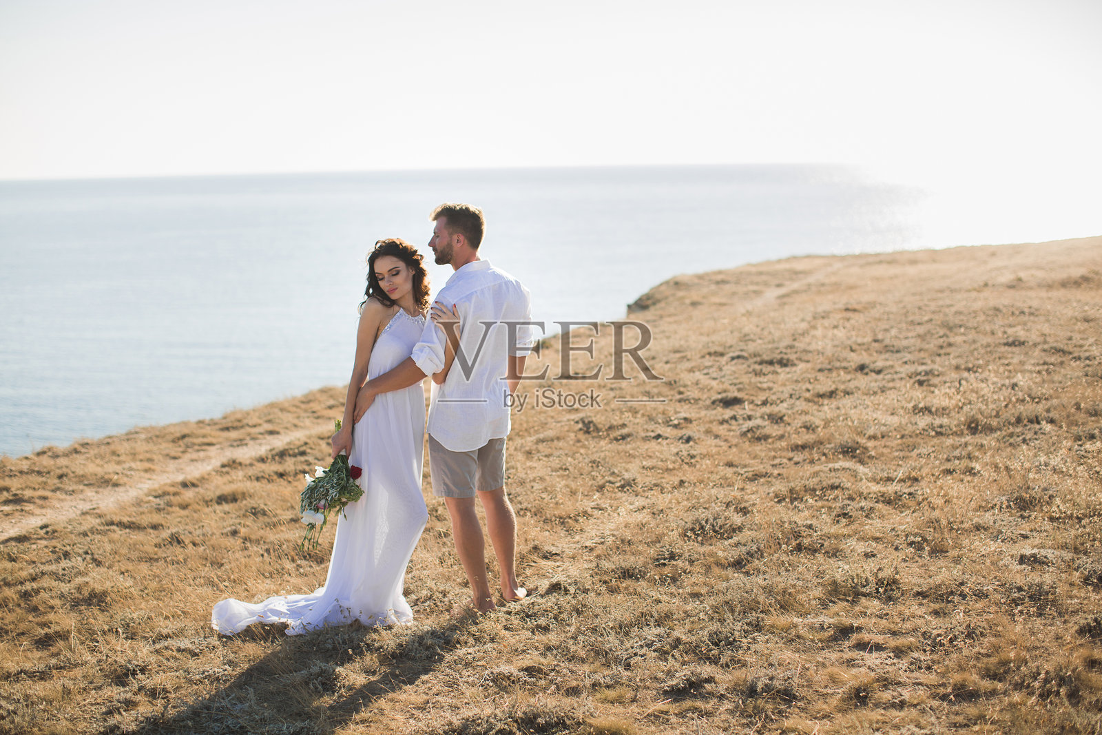 美丽的年轻情侣站在山崖边缘，身穿白色长袍。照片摄影图片