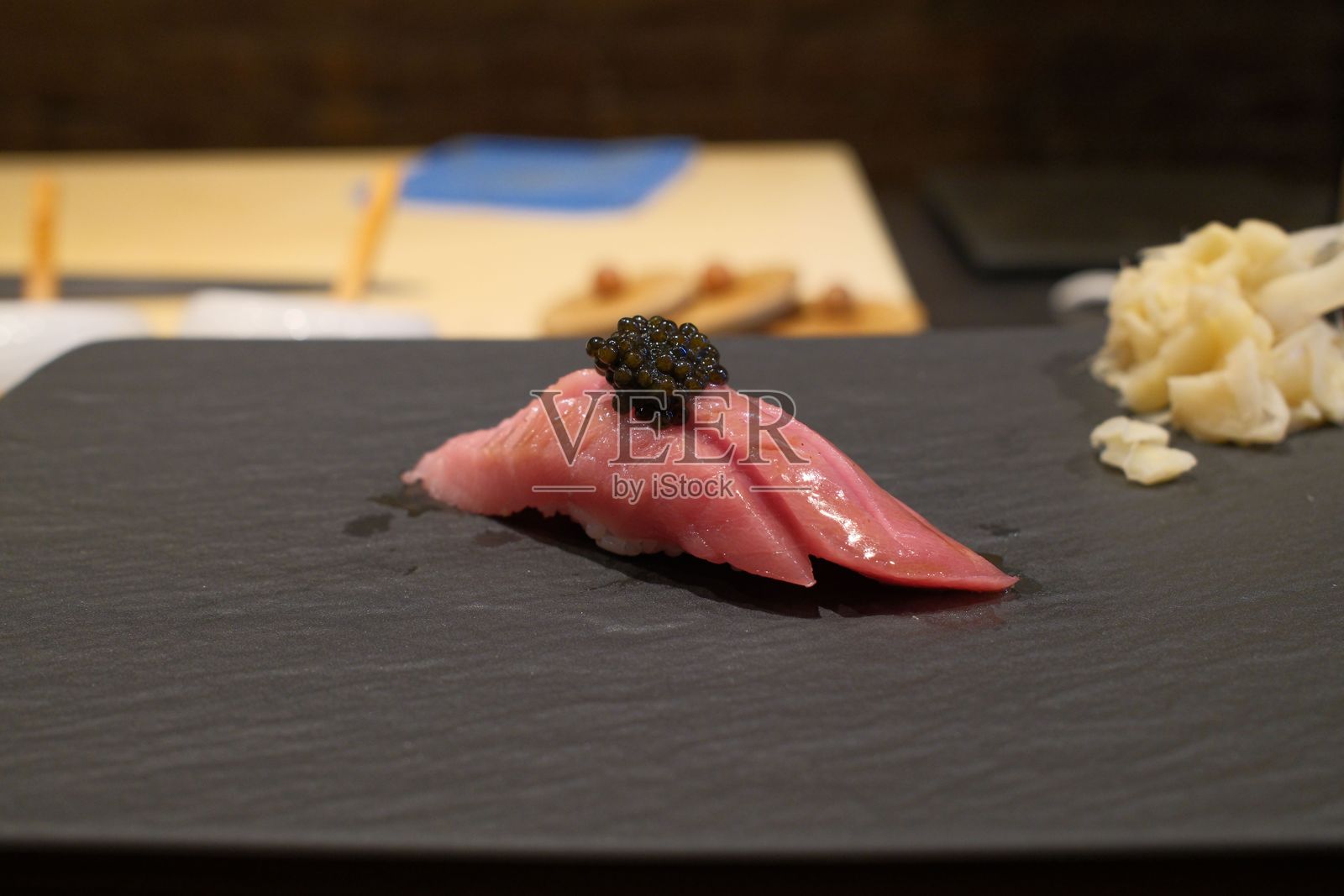 黑色石板上放着一块顶上有鱼子酱的寿司，旁边有姜片装饰。照片摄影图片