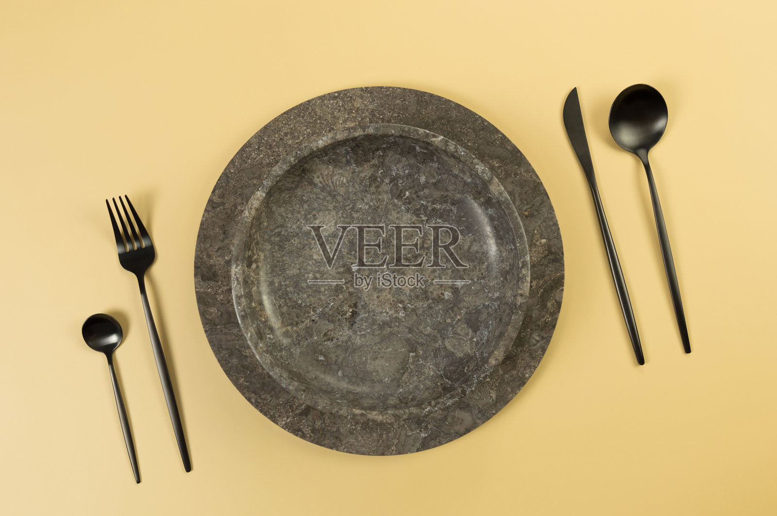 棕色大理石托盘和盘子的俯视图，黑色餐具放在黄色背景上。食品展示，石材托盘。照片摄影图片
