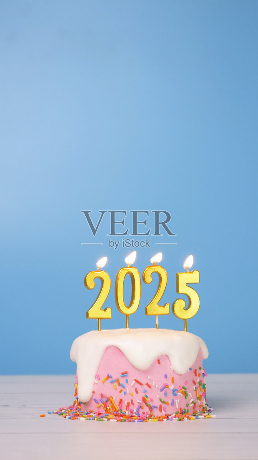 2025年快乐，新年庆祝派对上可爱的蛋糕上点燃了金色蜡烛数字2025。蜡烛的火焰在蓝色背景下摇曳闪烁，呈现出竖向构图。照片摄影图片