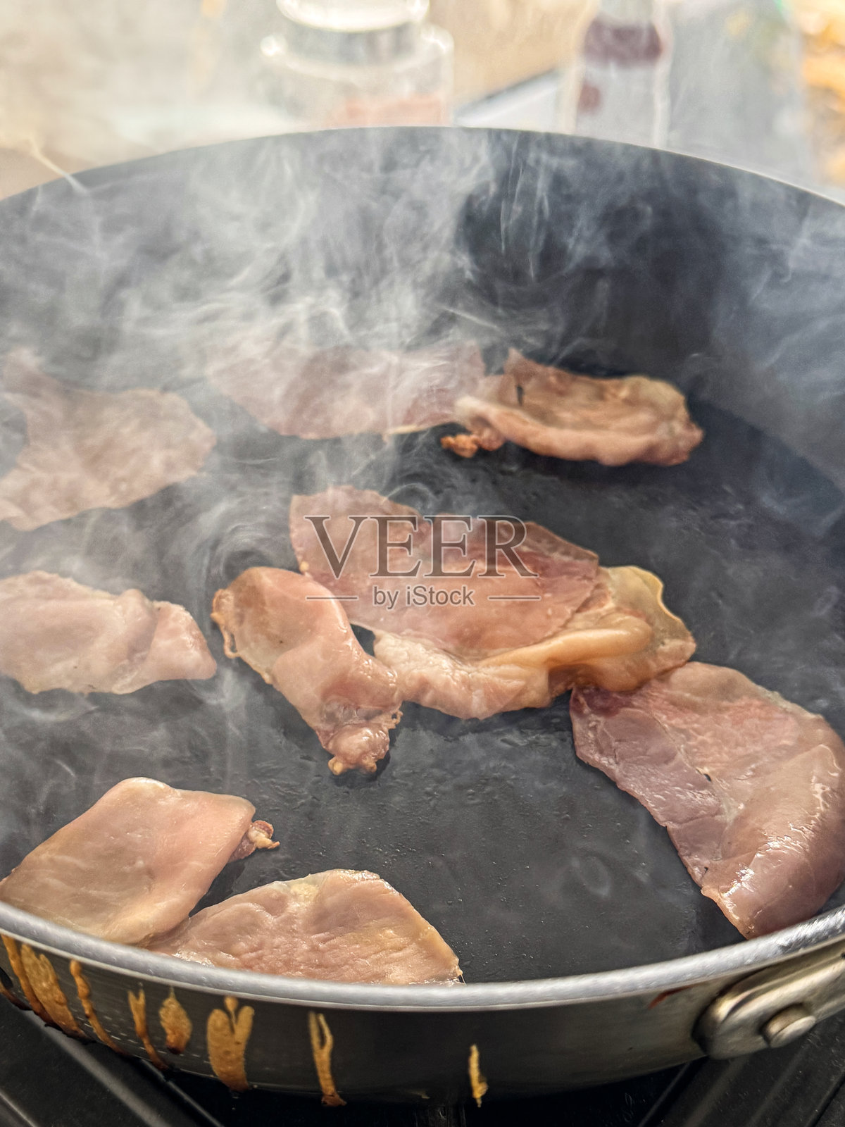 特写镜头，干煎无皮培根条在冒烟的不粘锅中烹饪，厨房环境背景，俯视角度，重点在前景。照片摄影图片