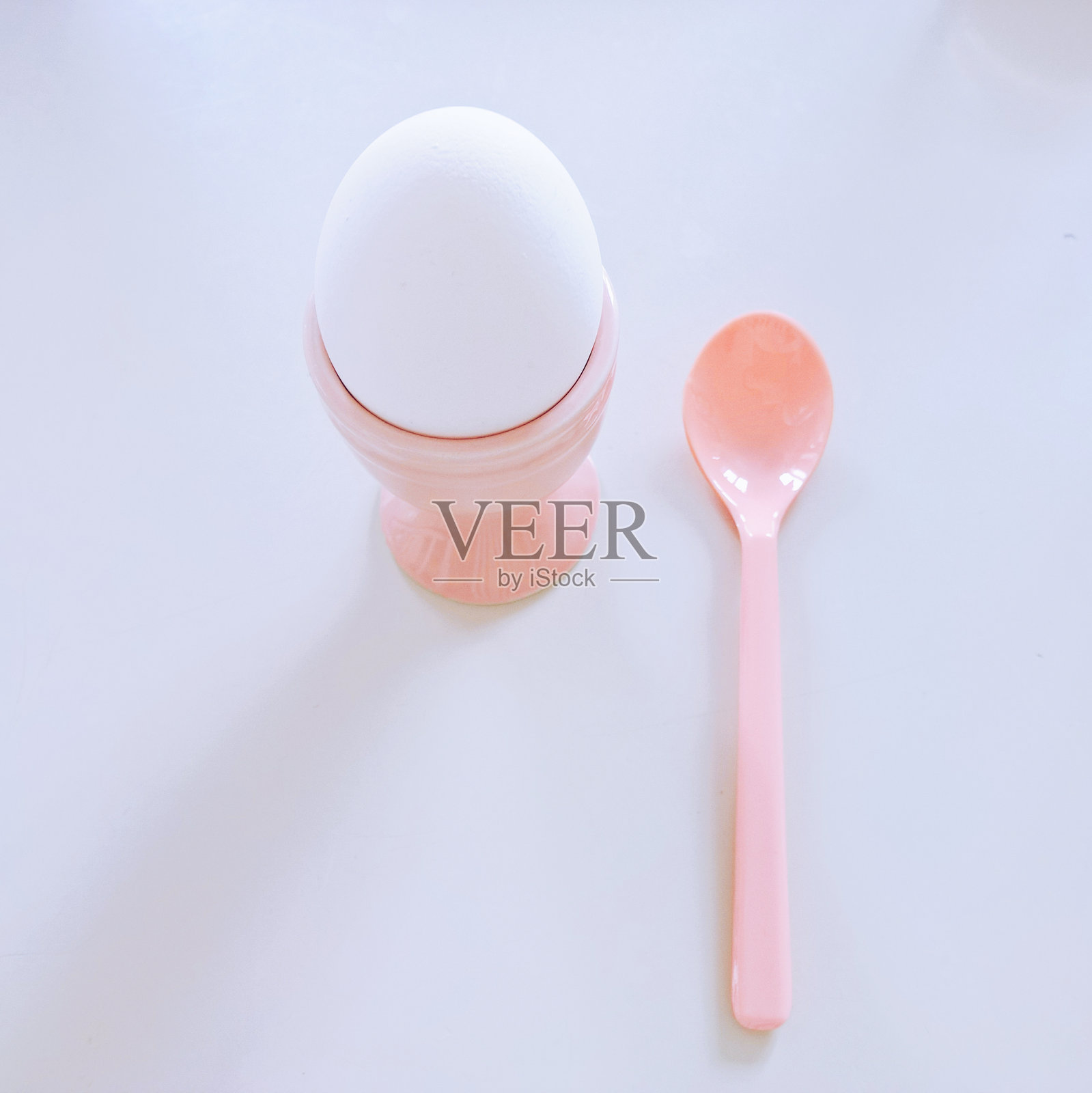 白色背景下，勺子旁边的杯子里的鸡蛋俯视图照片摄影图片