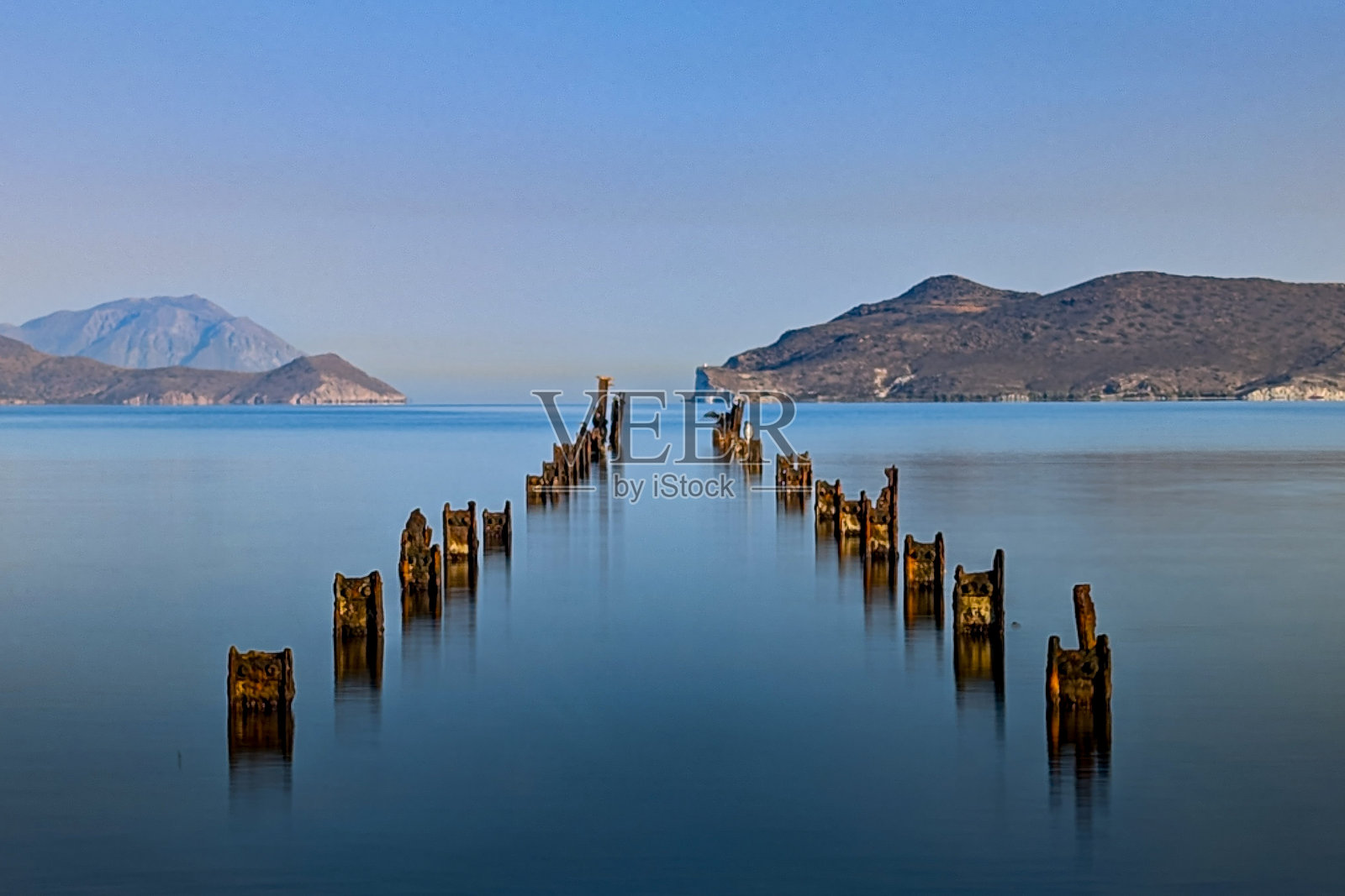 米洛斯岛海湾的长时间曝光图像，废弃的码头遗迹和几只鸟栖息在柱子上。照片摄影图片