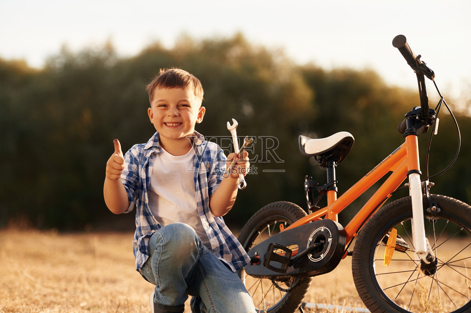 修理自行车，手握扳手。可爱的男孩在田野上与他的自行车在一起。照片摄影图片