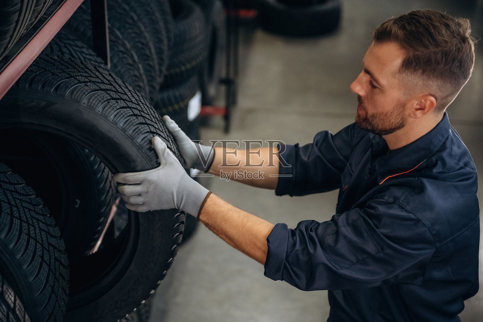 戴着灰色手套的工人在维修站处理轮胎。照片摄影图片