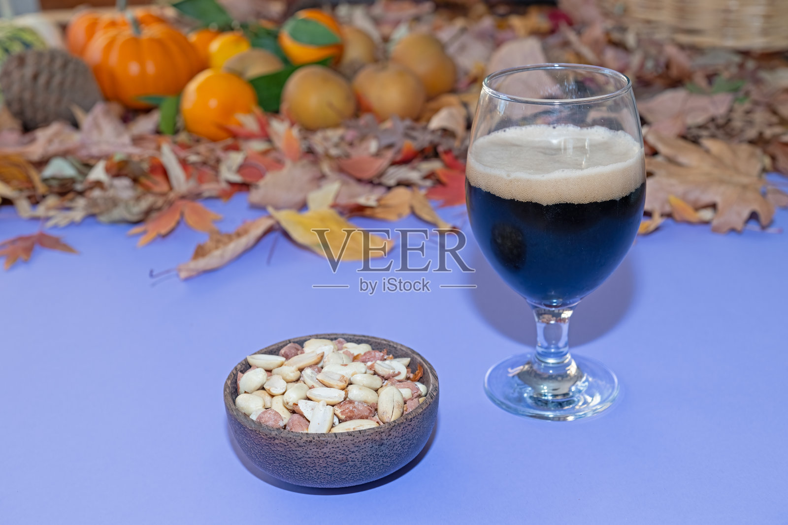 黑啤酒和一碗烤花生，桌上还有秋天的落叶和水果。照片摄影图片