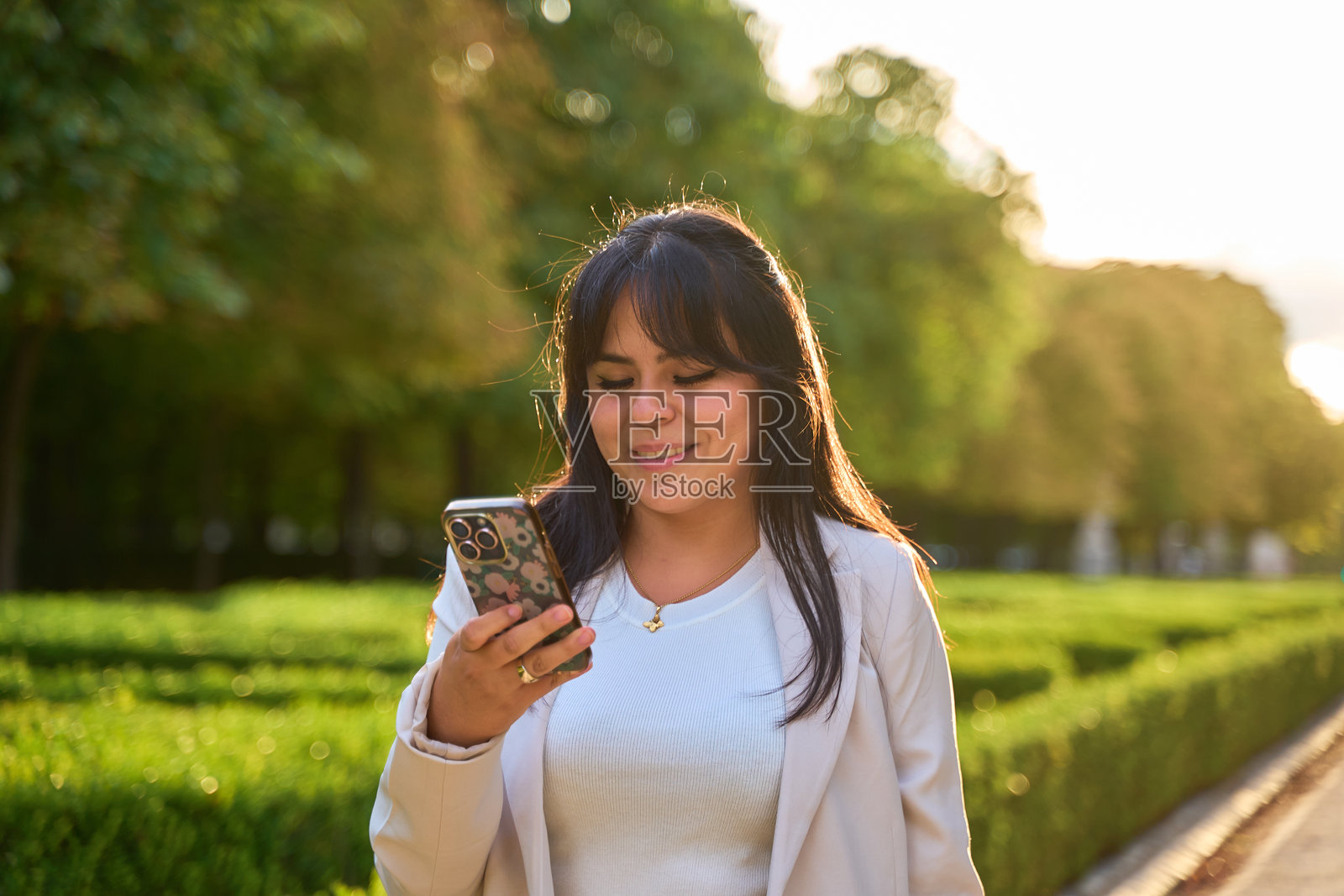 在阳光明媚的公园里，一位拉丁裔女性微笑着使用手机。照片摄影图片