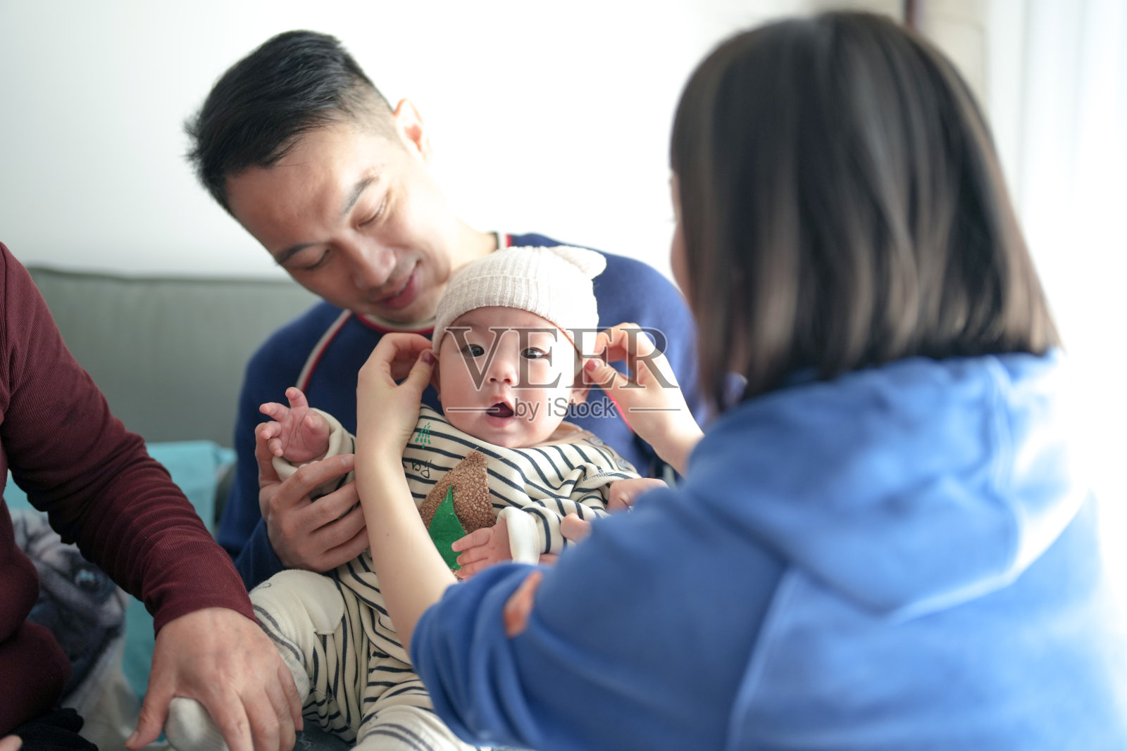 一个6个月大的男孩穿着圣诞服装，在寒冷的冬天与他的父亲、母亲和祖母一起在上海浦东新区的室内度过时光。照片摄影图片