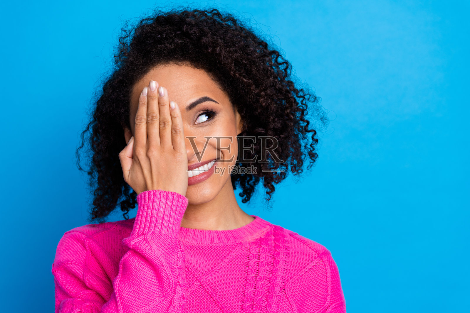 漂亮年轻女士的肖像，手臂遮住眼睛，凝视空旷的空间，穿着粉色毛衣，背景为蓝色。照片摄影图片