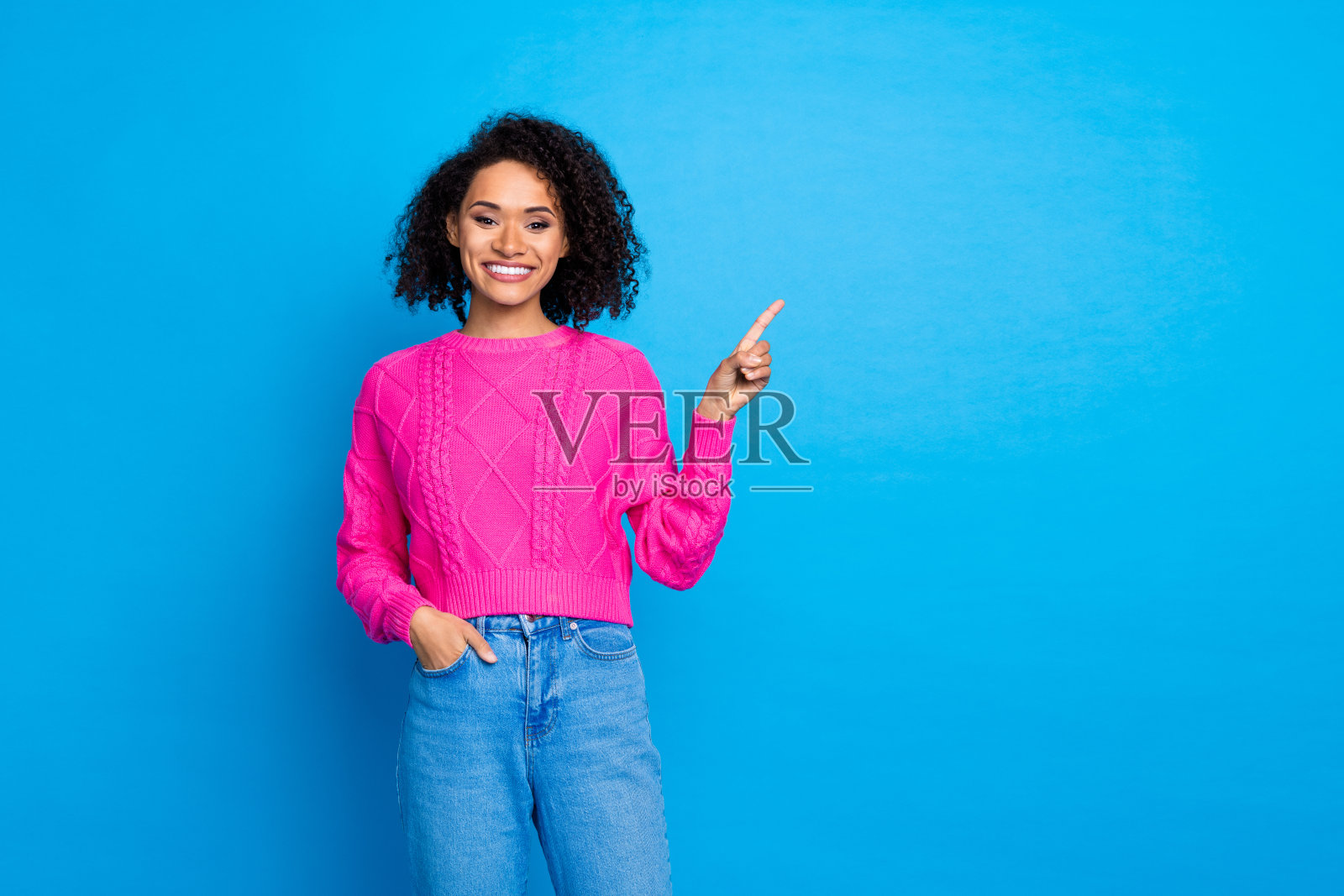 漂亮年轻女士的肖像，手指指向空白处，穿着粉色毛衣，背景为蓝色。照片摄影图片