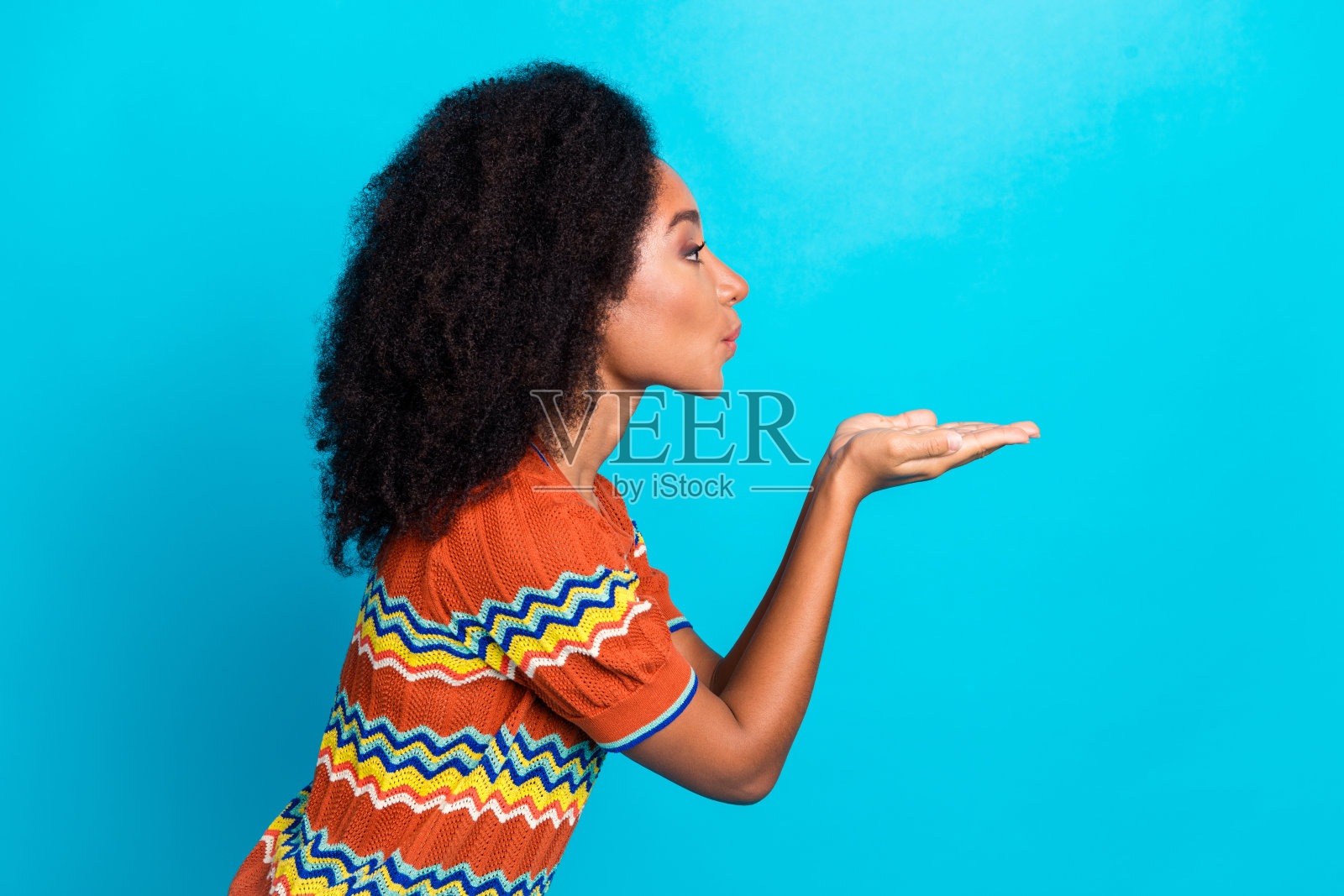 迷人的年轻女性穿着彩色条纹T恤，手势俏皮地摆姿势，背景为鲜艳的蓝色。照片摄影图片