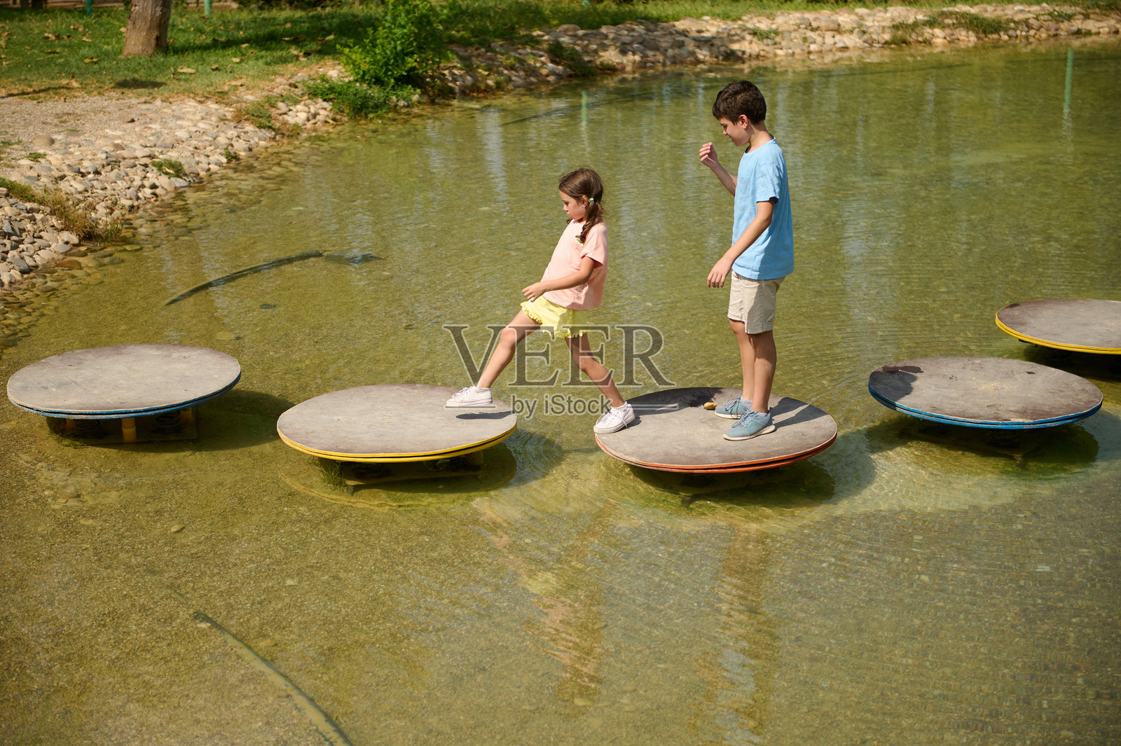孩子们在户外的浅水塘上平衡着走过石头。照片摄影图片