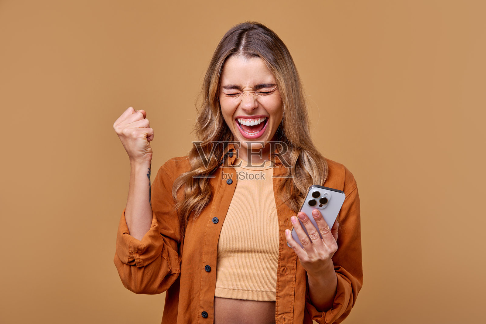 一位兴奋的年轻女性高兴地庆祝，同时紧握着她的智能手机。照片摄影图片