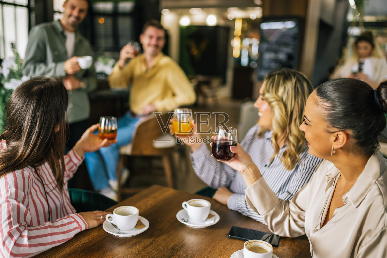 一群女性朋友在餐厅喝咖啡，后面的男生试图给她们送饮料。女孩们咯咯笑着，聊起了他们。照片摄影图片