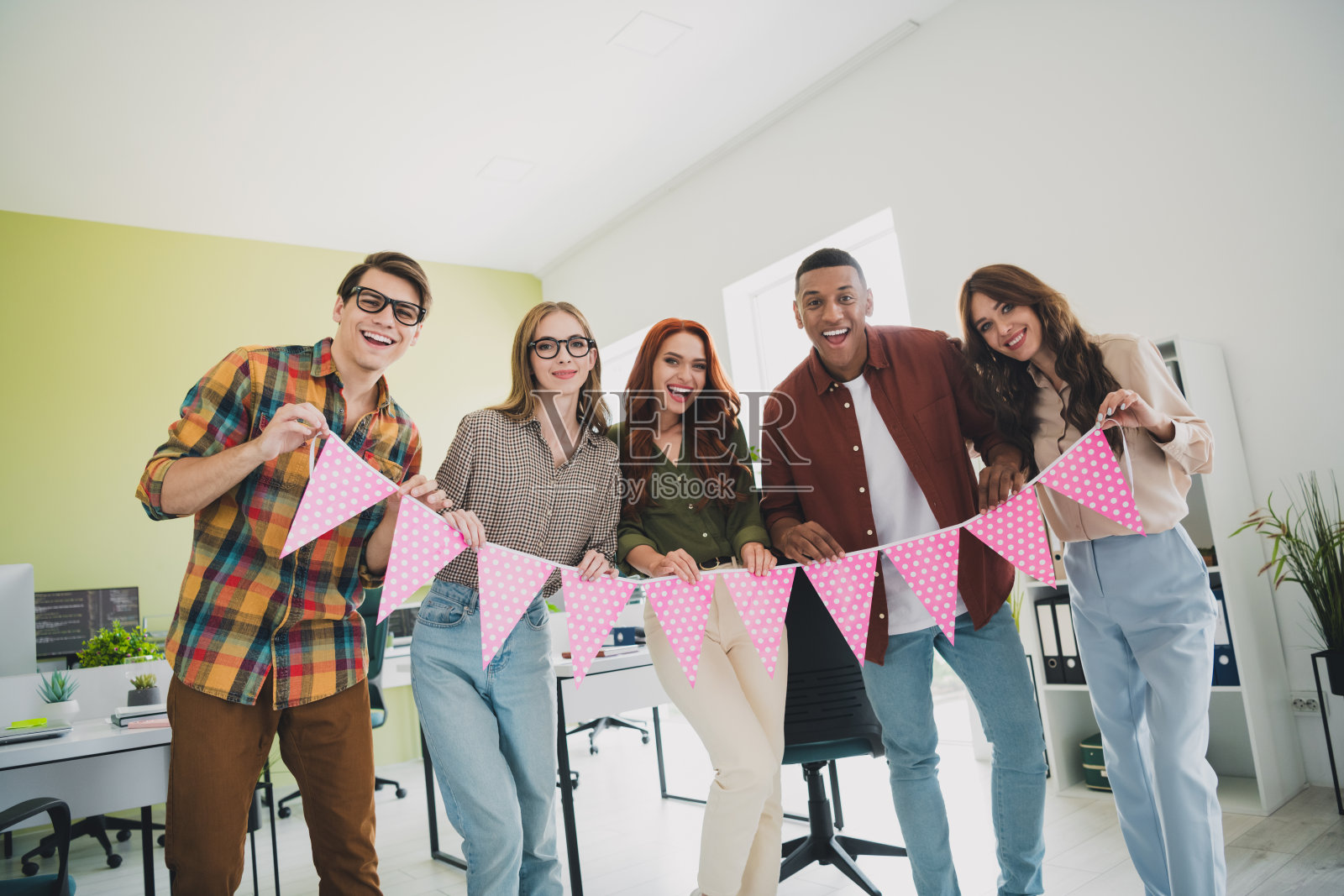 年轻成功的经理们，男女多样化，手持粉色旗帜装饰，庆祝公司周年纪念在办公室。照片摄影图片