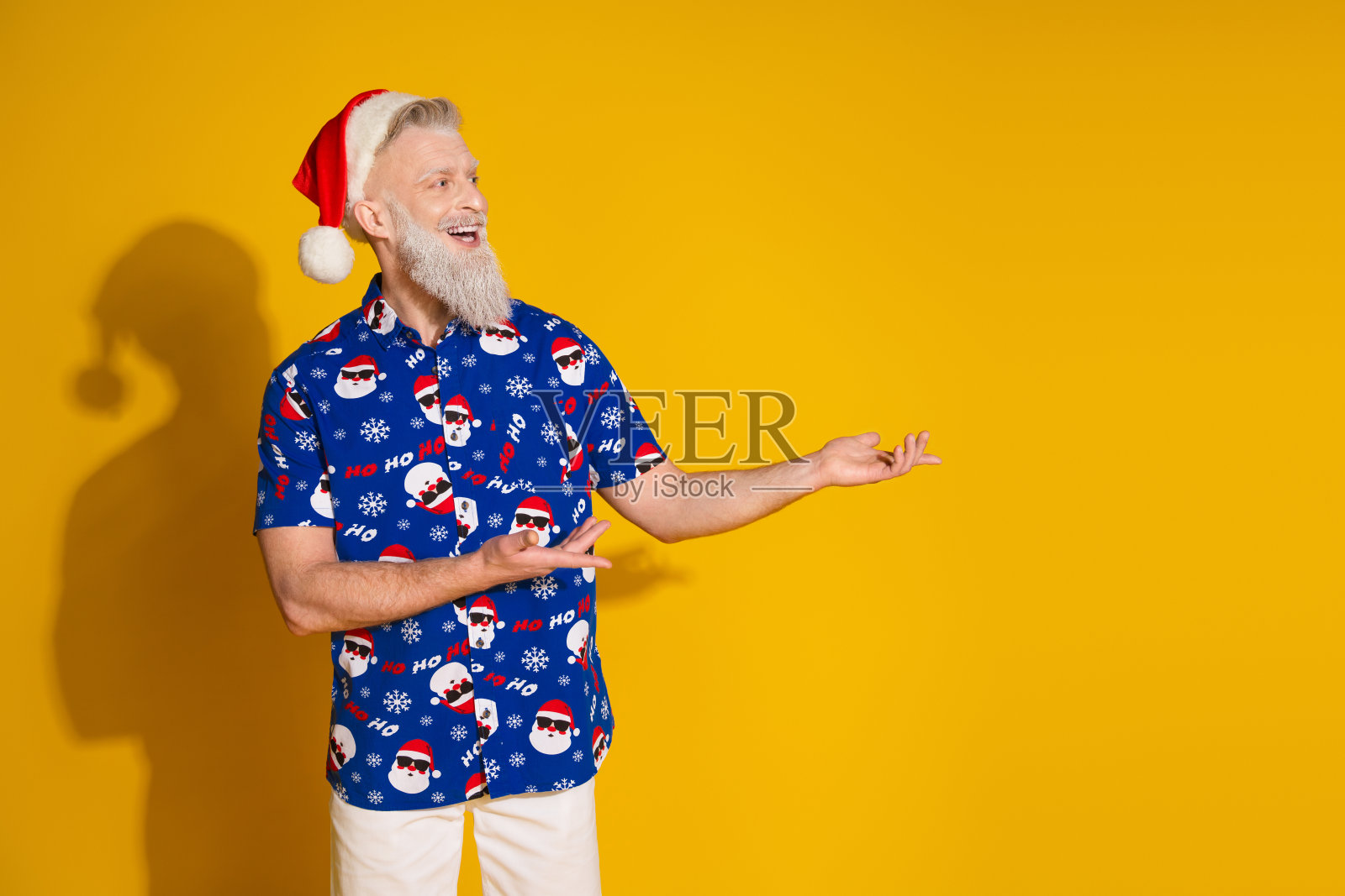 搞笑时尚的圣诞老人手臂展示空白空间，穿着冬季圣诞印花衬衫，背景为黄色。照片摄影图片