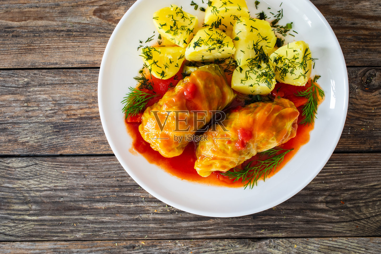 用卷心菜叶包裹的肉末，配以番茄酱和煮土豆，摆放在白色盘子上，放在木桌上 - 波兰菜肴戈旺基。照片摄影图片