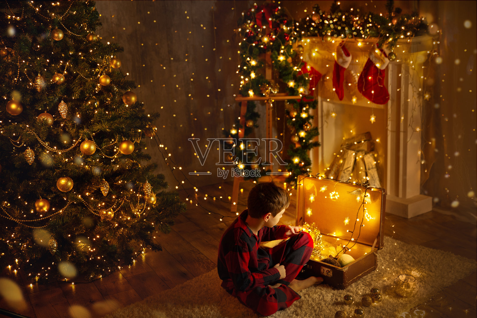 圣诞房间背景，壁炉和圣诞树灯光。小孩在复古行李箱中打开圣诞礼物。温馨的圣诞家居装饰。照片摄影图片