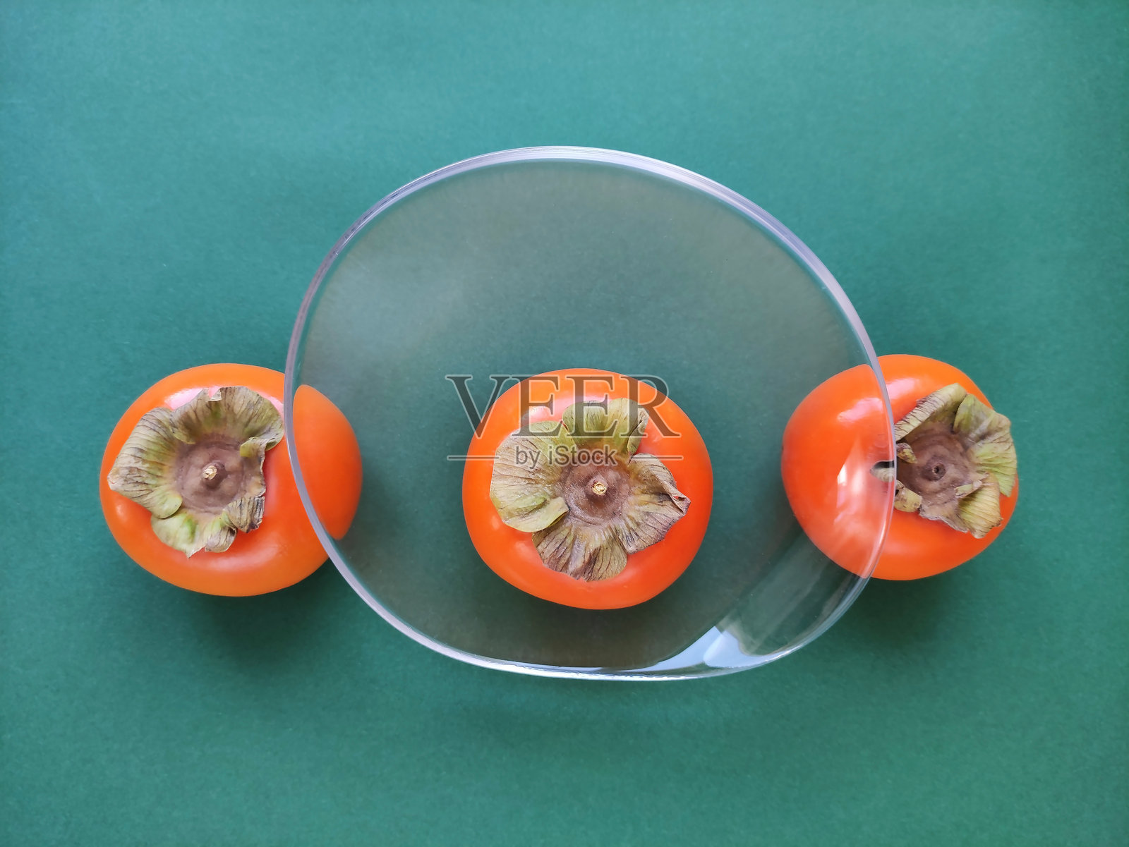 新鲜自然的圆形橙色柿子，带有绿色叶子，放在盘子里照片摄影图片