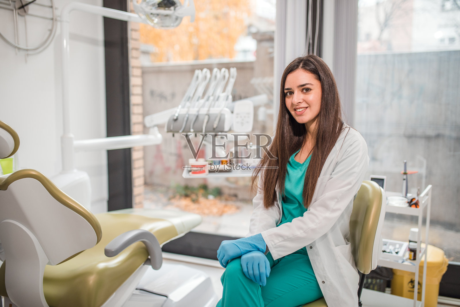 女牙医坐在牙科办公室里，直视镜头。照片摄影图片