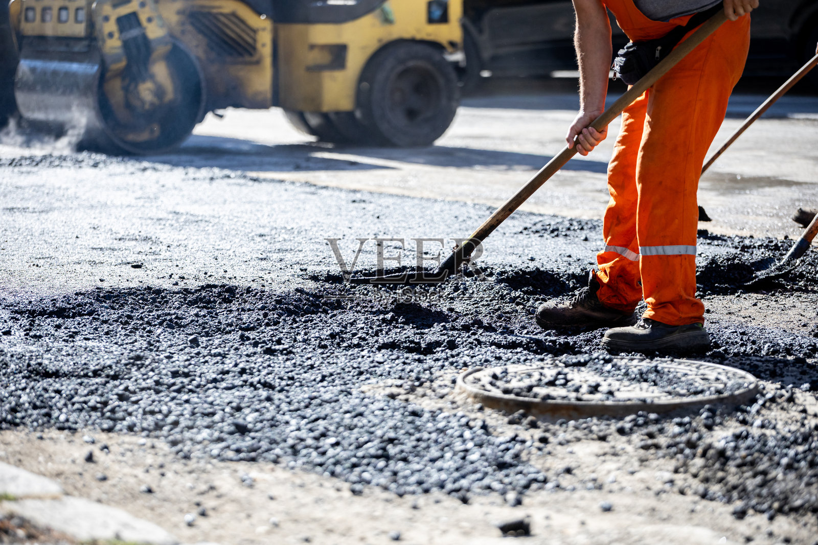 工人在明亮的白天使用沥青修复城市道路，展示了繁忙地点的施工努力照片摄影图片