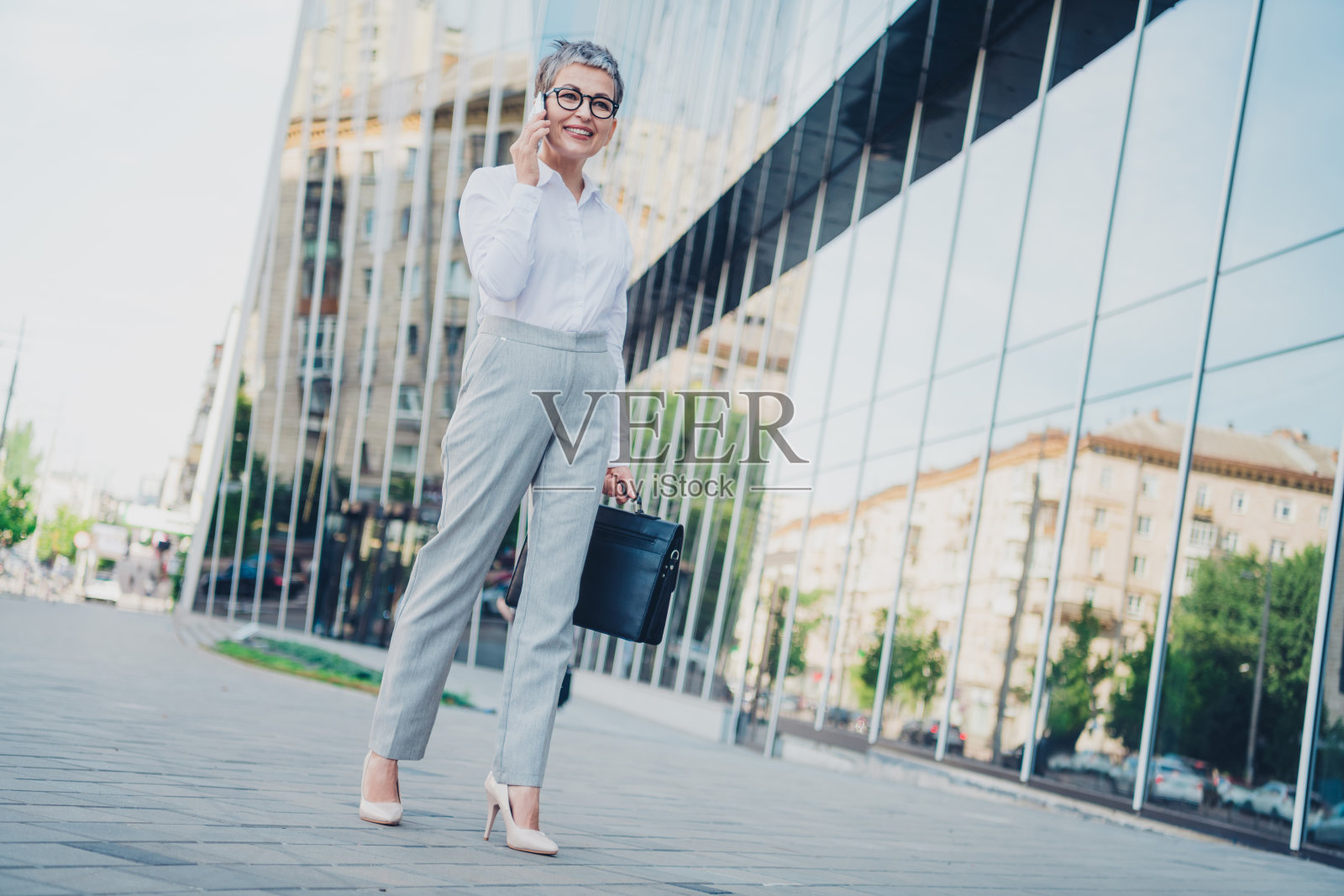 自信的成熟的女商人在城市户外站立，散发着成功的气息，穿着优雅的正式服装，手提公文包。照片摄影图片