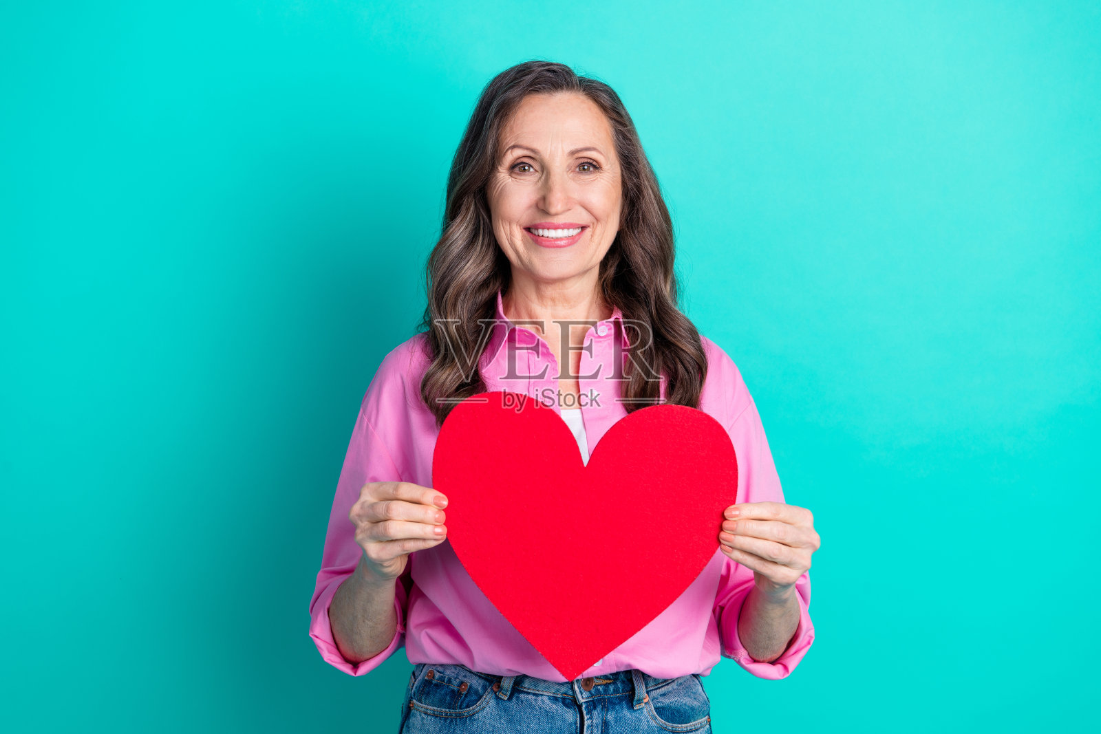 穿着粉色衬衫的迷人女士手持大红心，背景为清新的蓝绿色，留有空白空间。照片摄影图片