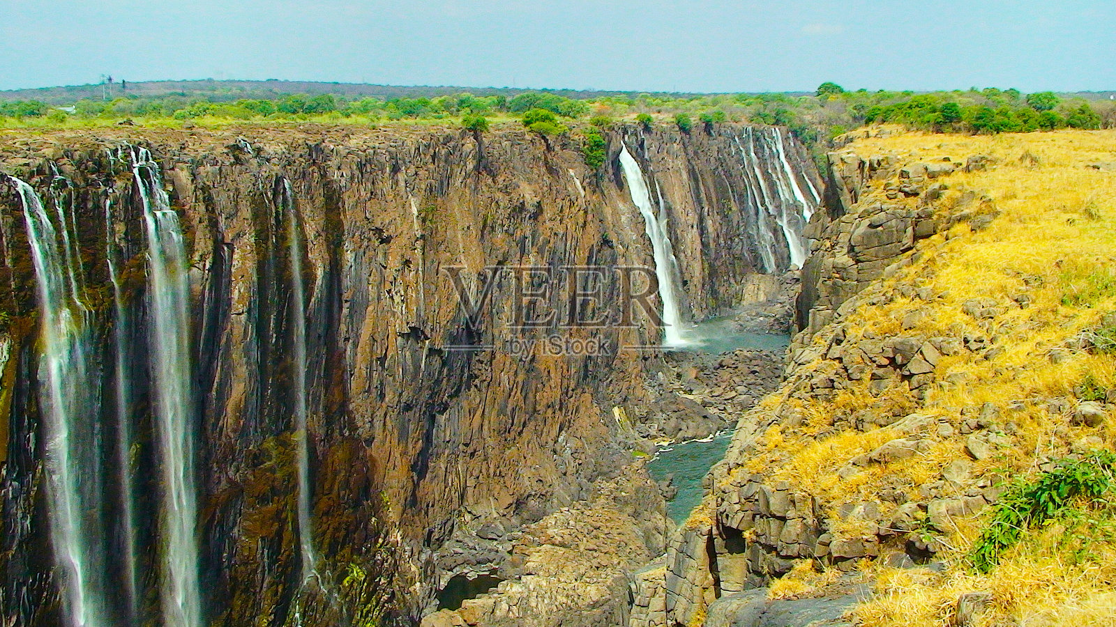 戏剧性的瀑布从崎岖的岩石悬崖边缘倾泻而下，落入深邃的峡谷。照片摄影图片