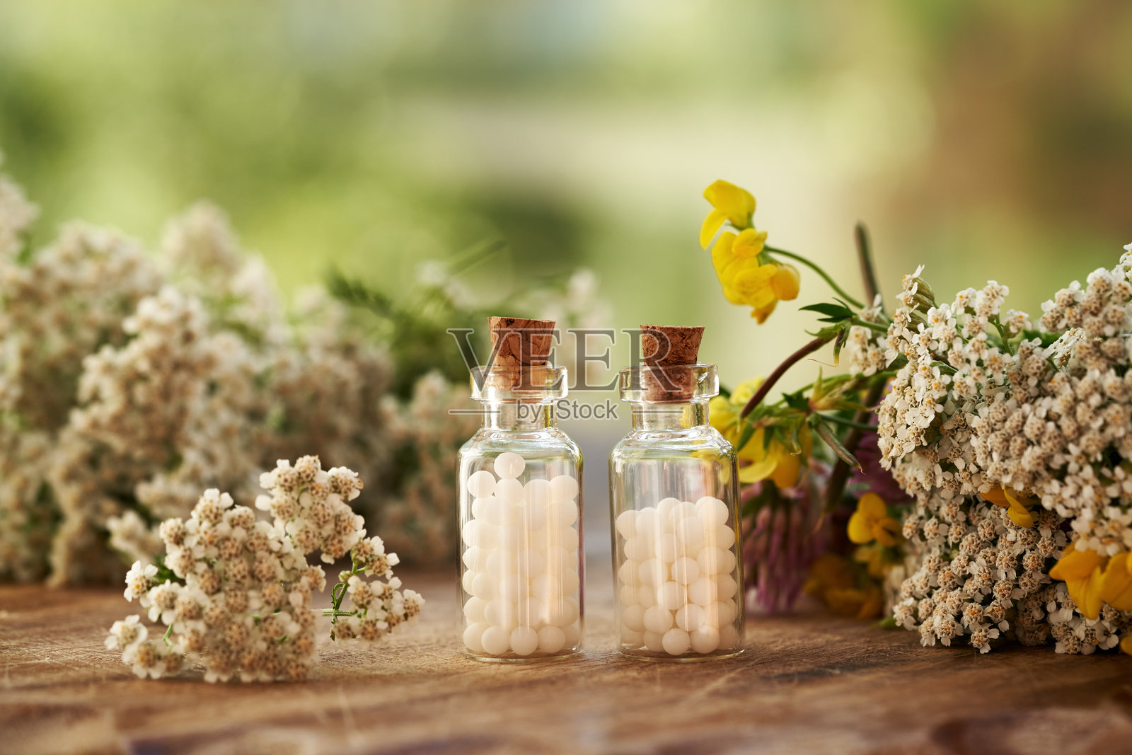 两瓶装有白色顺势疗法小球的玻璃瓶，里面有蓍草和其他夏季花卉照片摄影图片