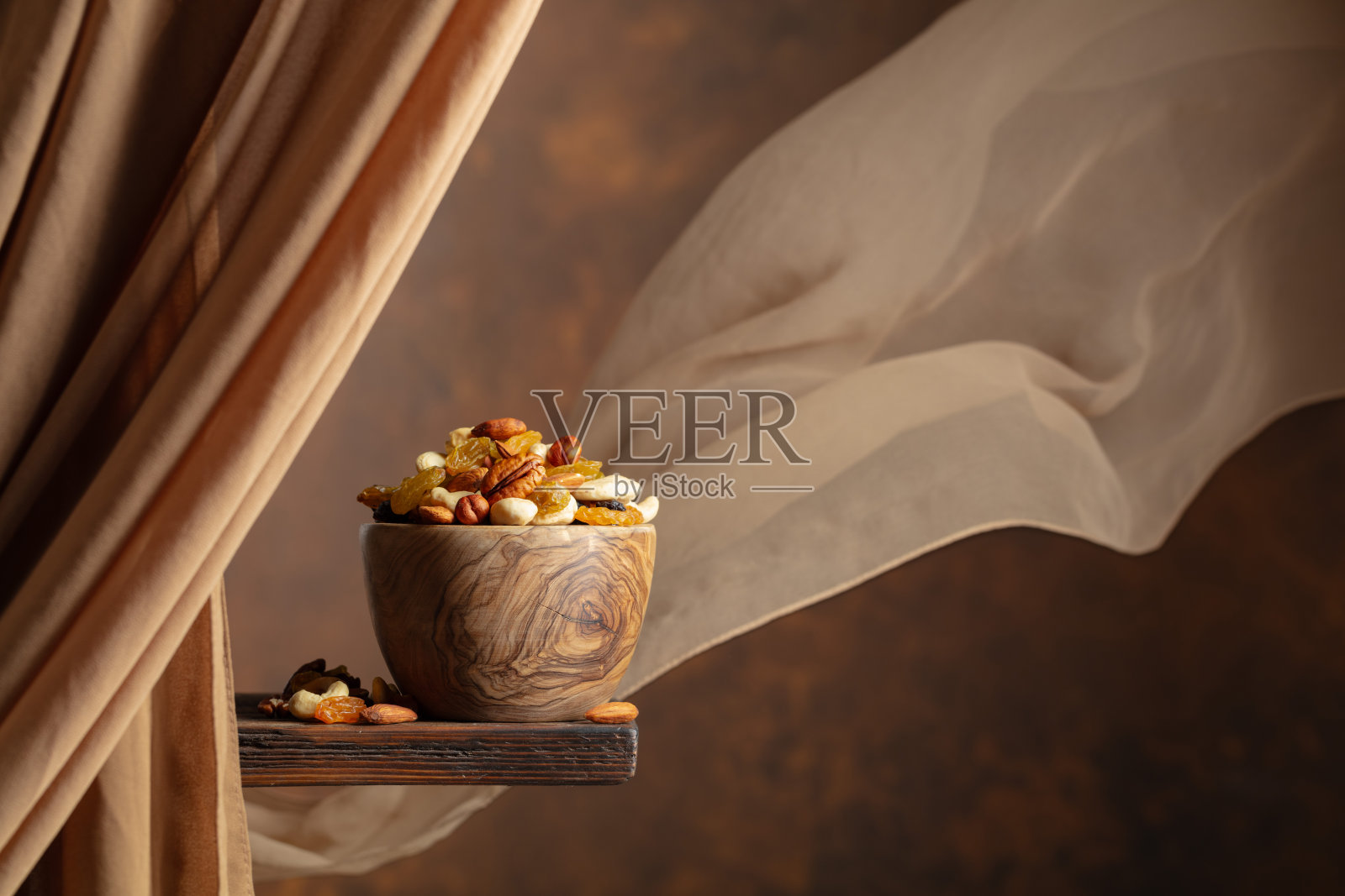 木碗中盛放着各种坚果和葡萄干，背景为棕色。照片摄影图片